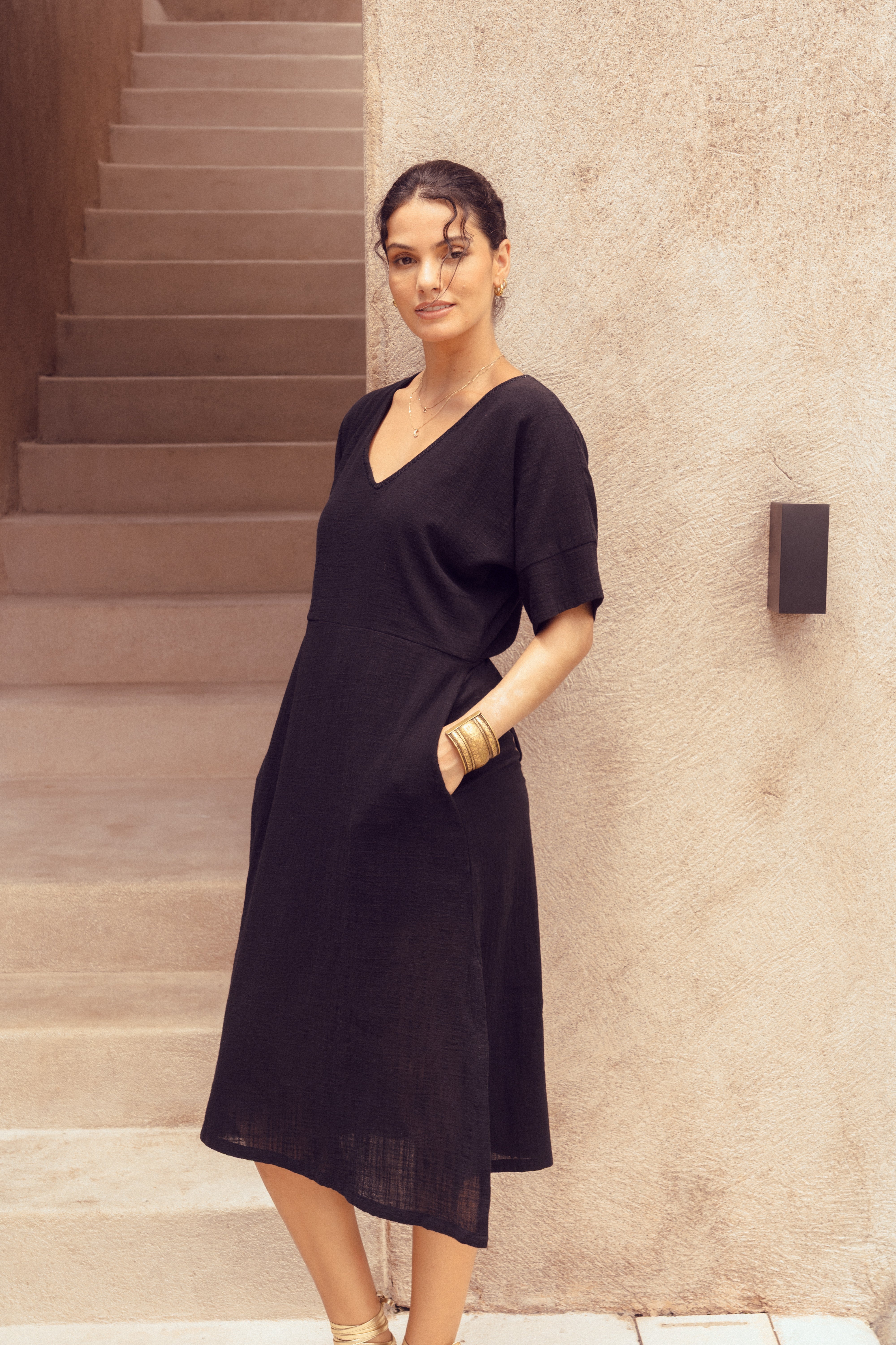 Woman in a black dress standing on steps against a beige wall.