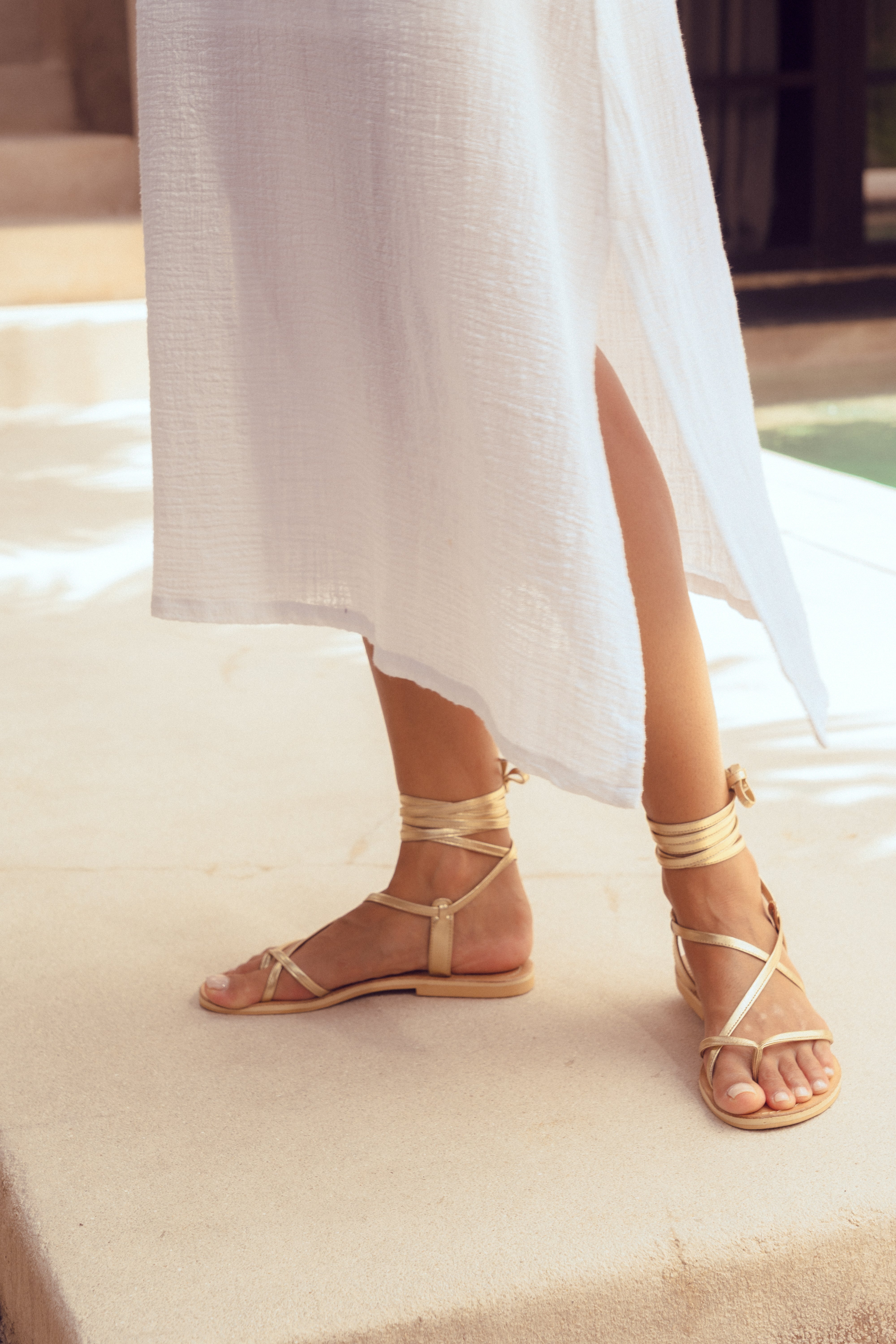 Person wearing gold sandals with white fabric in the background