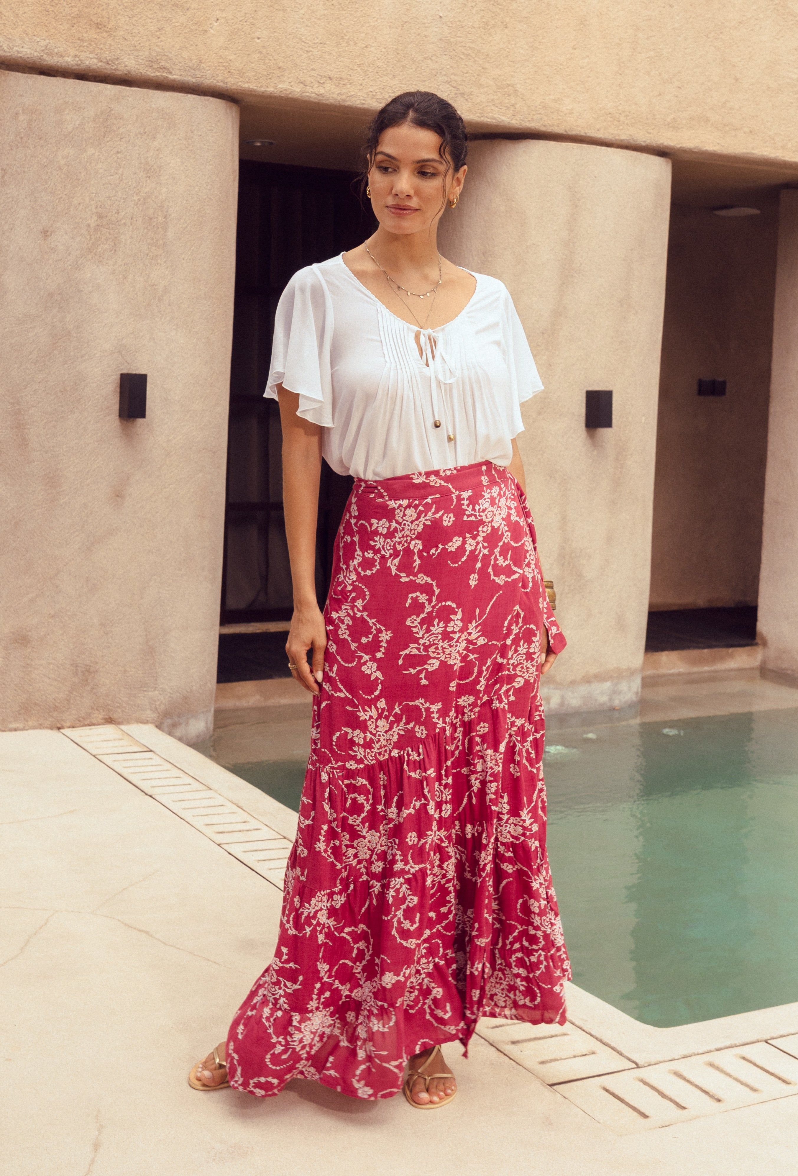Woman in a white blouse and pink floral skirt standing by a pool.