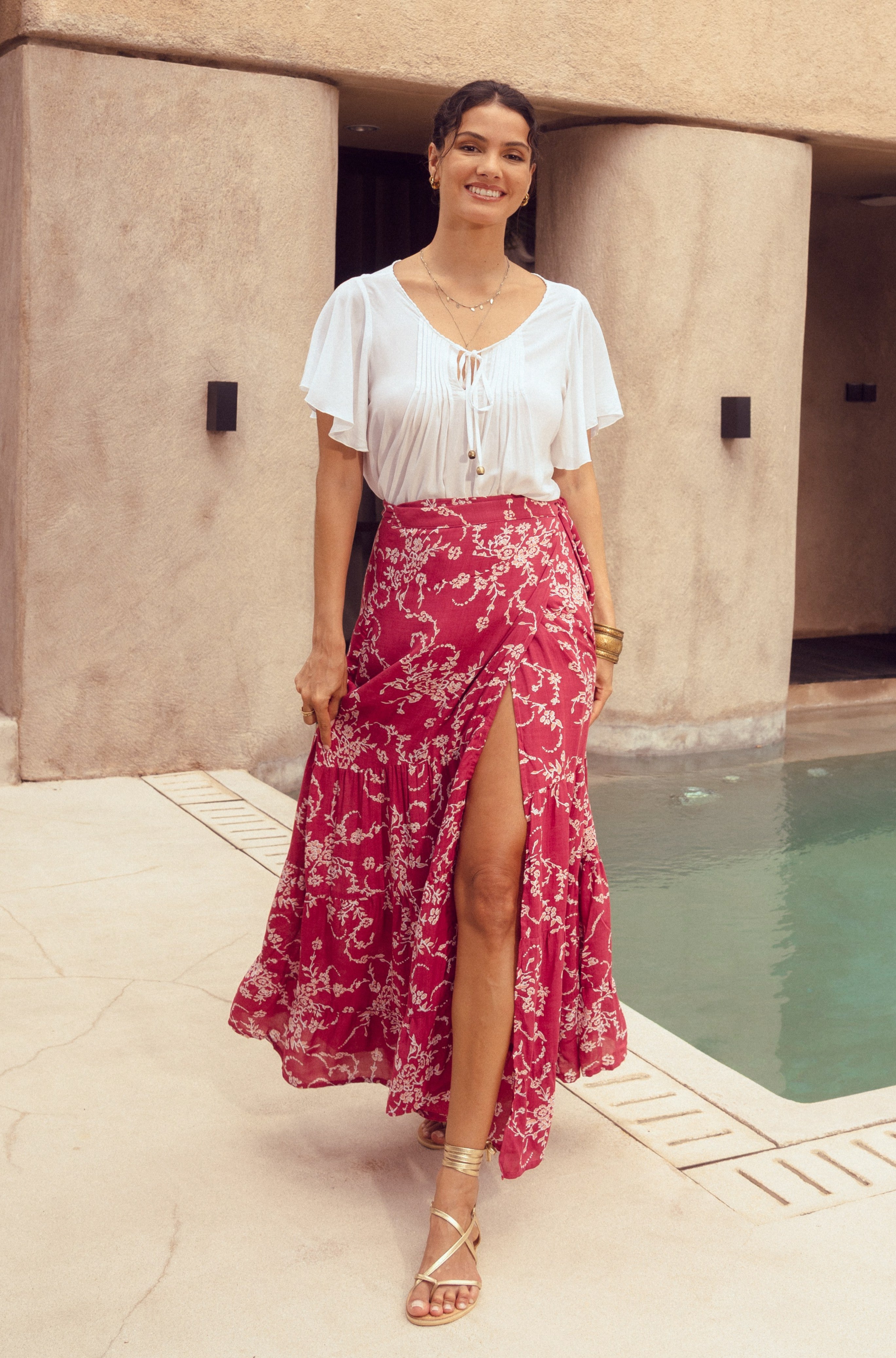 Woman in a white top and pink floral skirt standing by a pool.