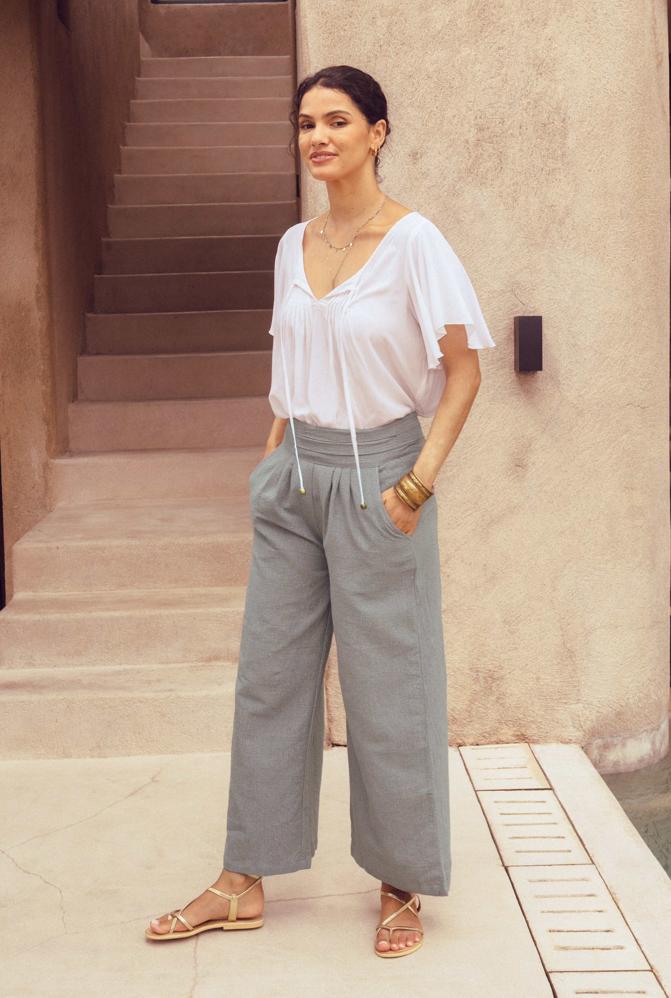 Woman wearing a white blouse and gray wide-leg pants standing in front of a building.