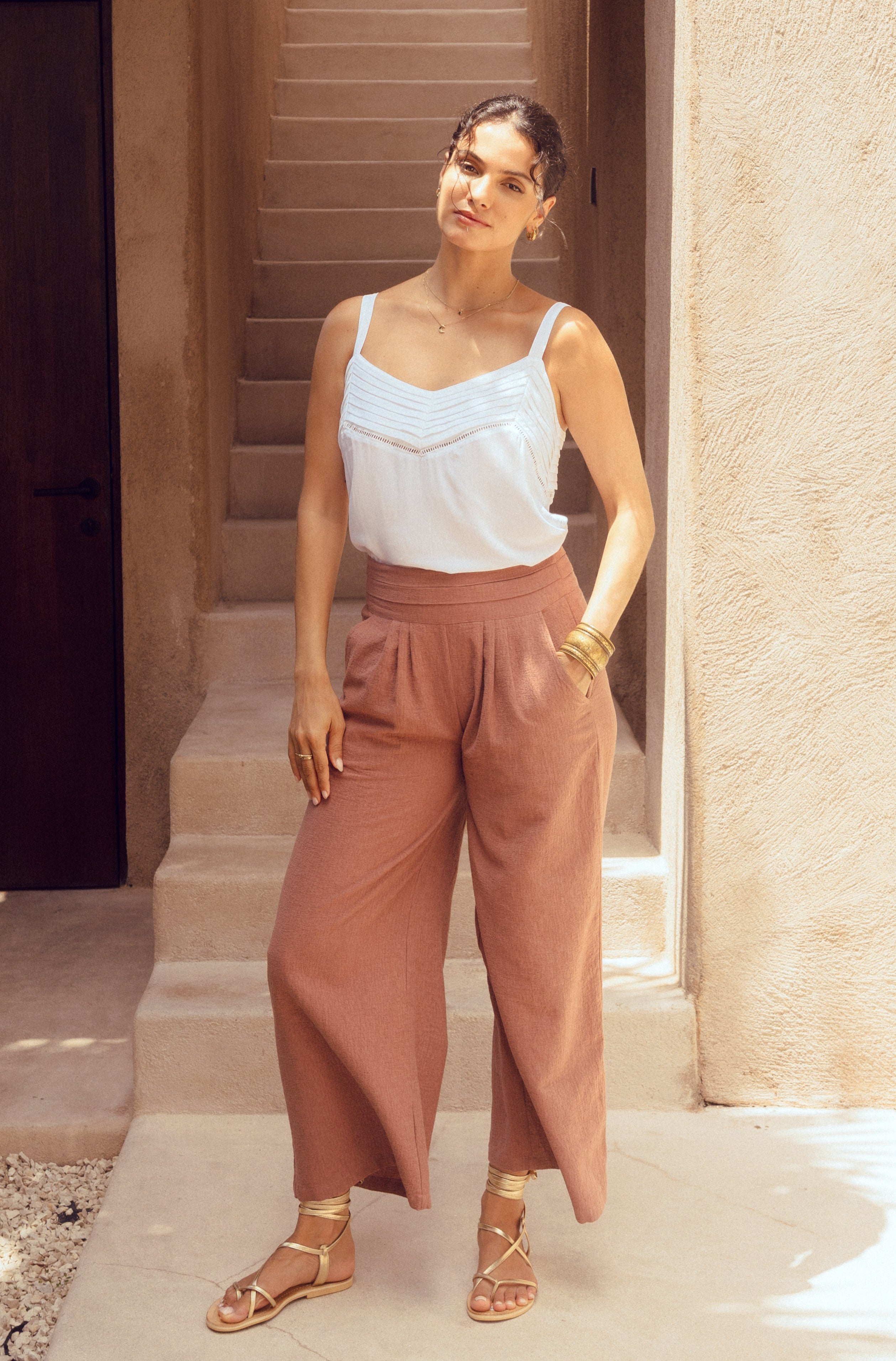 Woman in white top and pink pants standing outdoors near a building entrance.