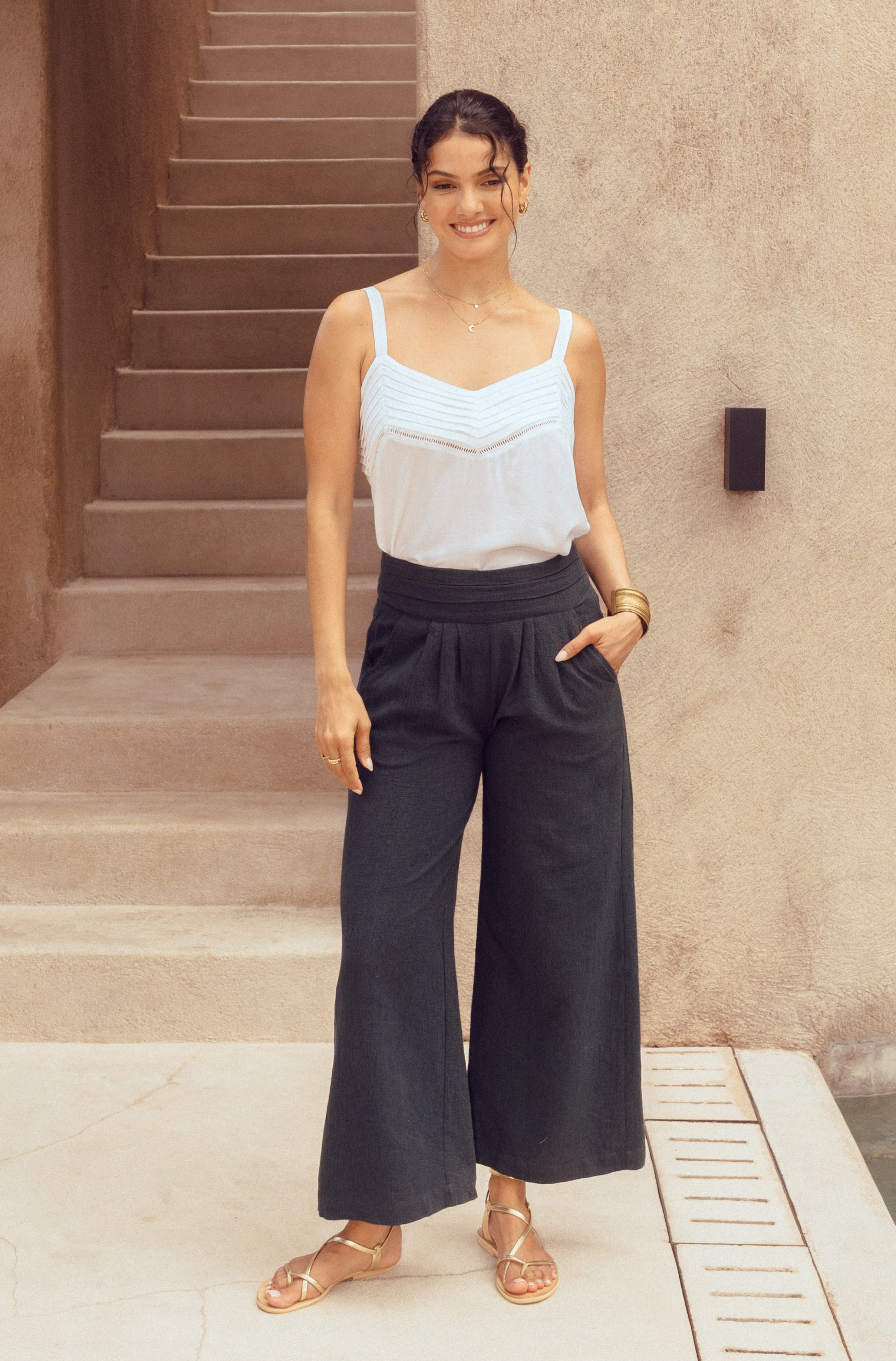 Woman in a light blue top and dark wide-leg pants standing on steps.
