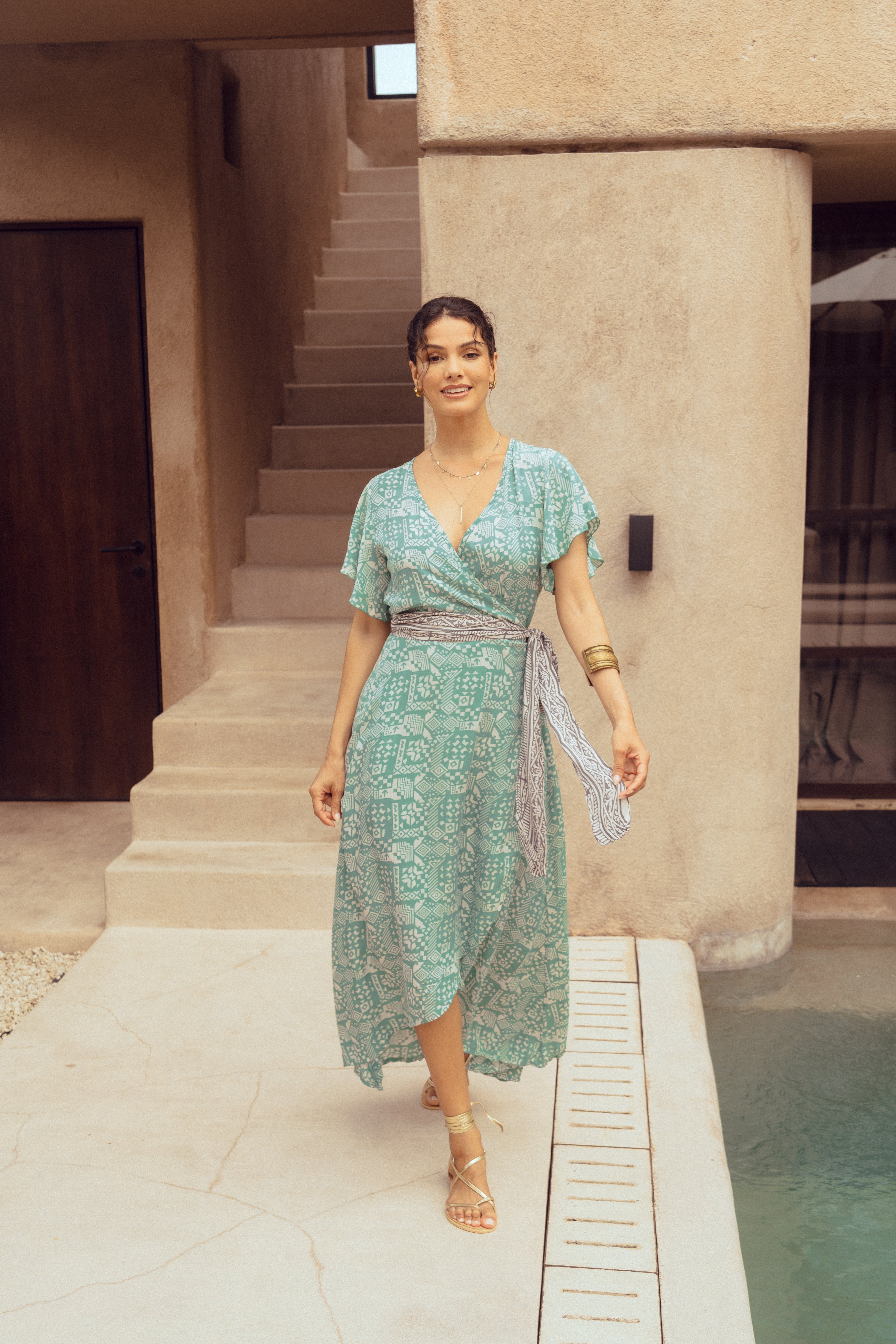 Woman in a green patterned dress standing by a poolside.