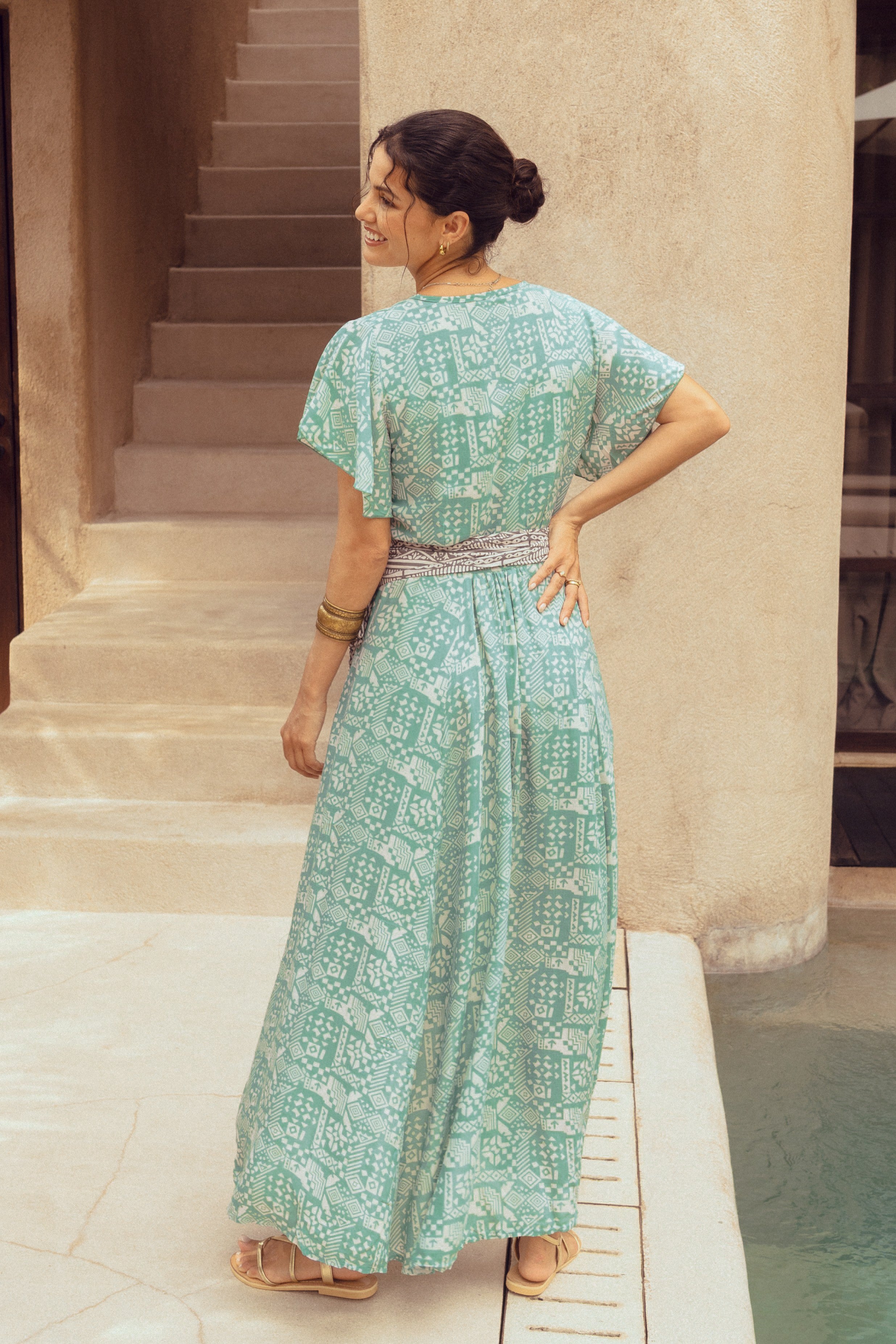 Woman in a green patterned dress standing by a poolside.
