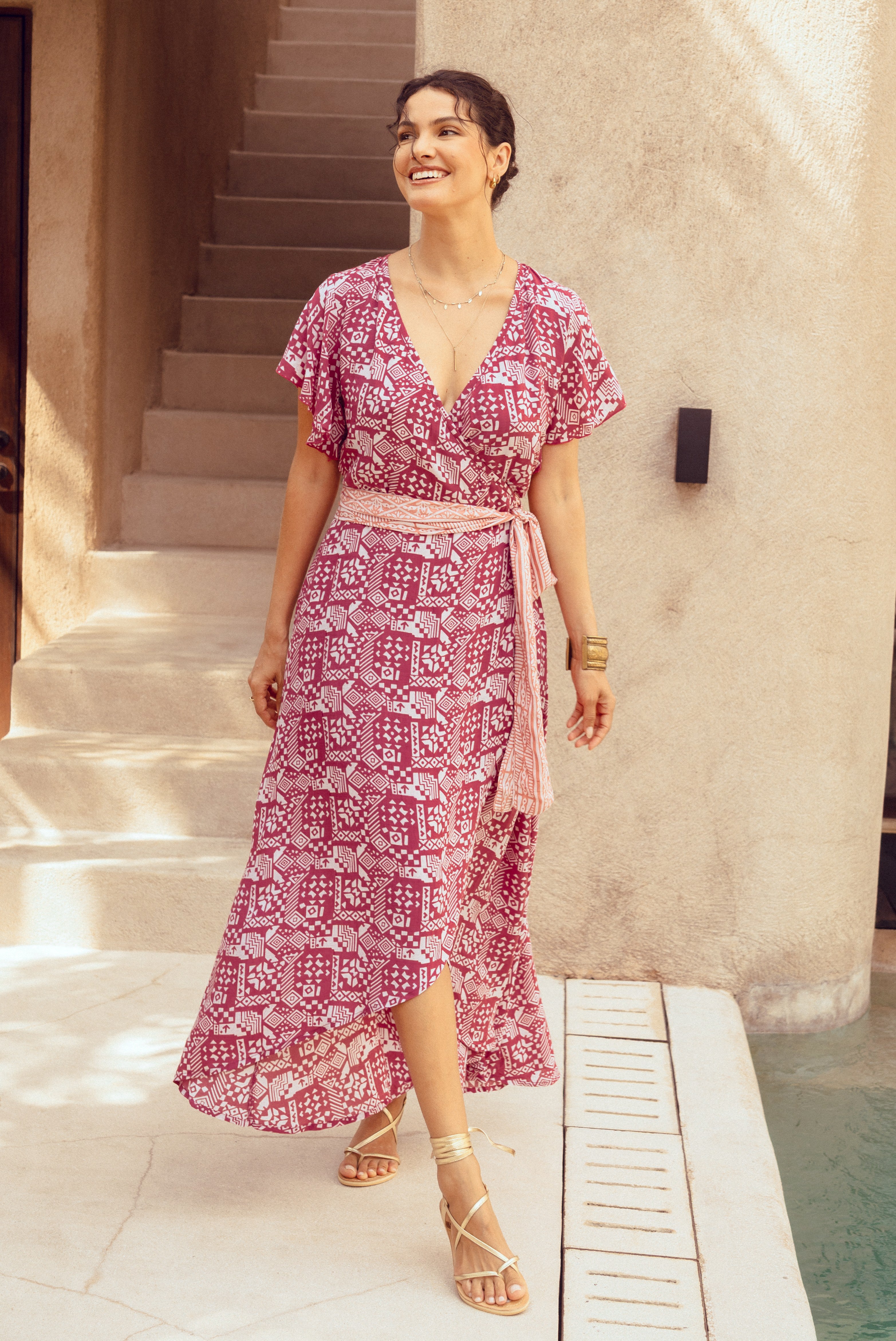 Woman in a pink patterned dress standing on a staircase near a pool.