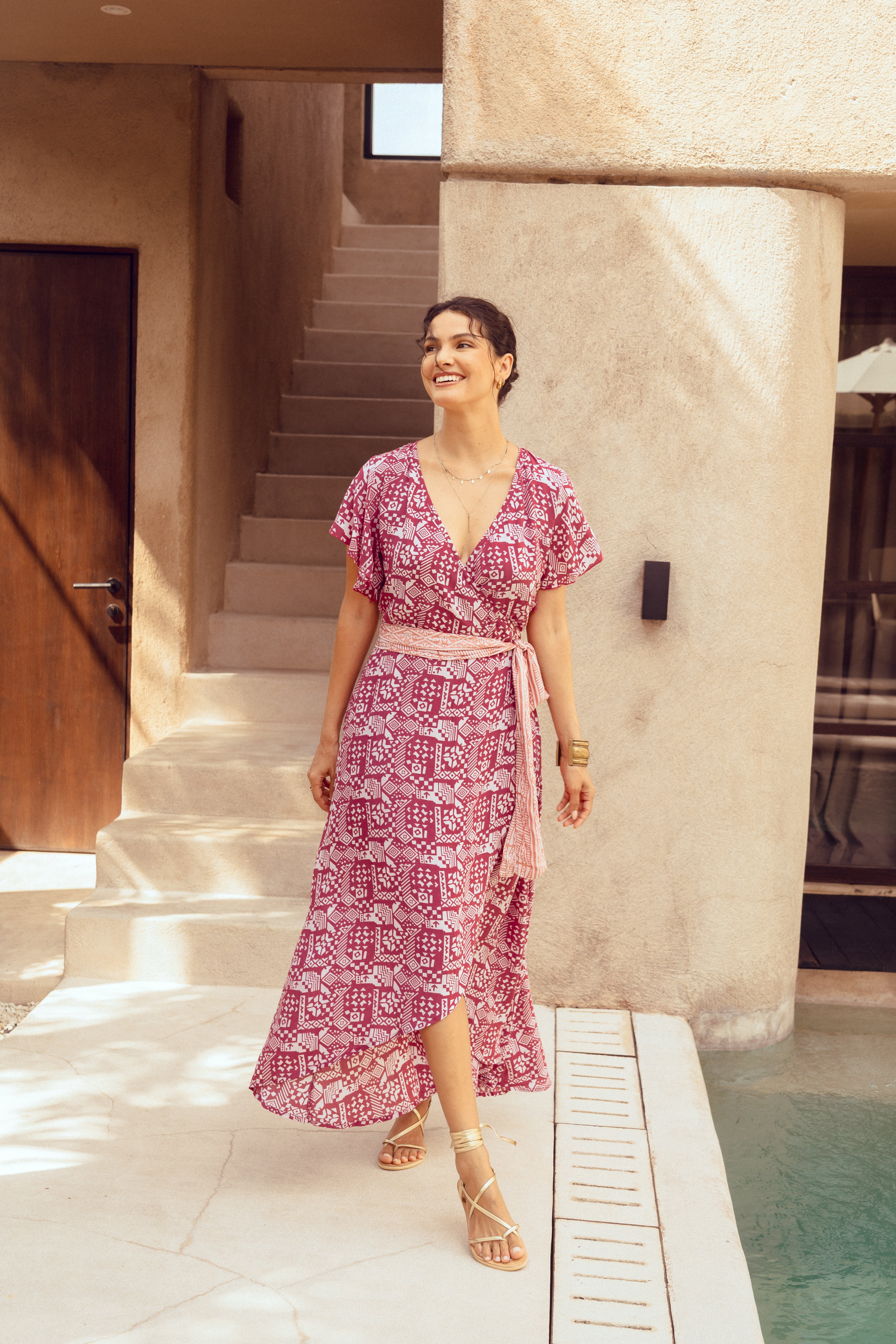 Woman in a pink patterned dress standing by a poolside.