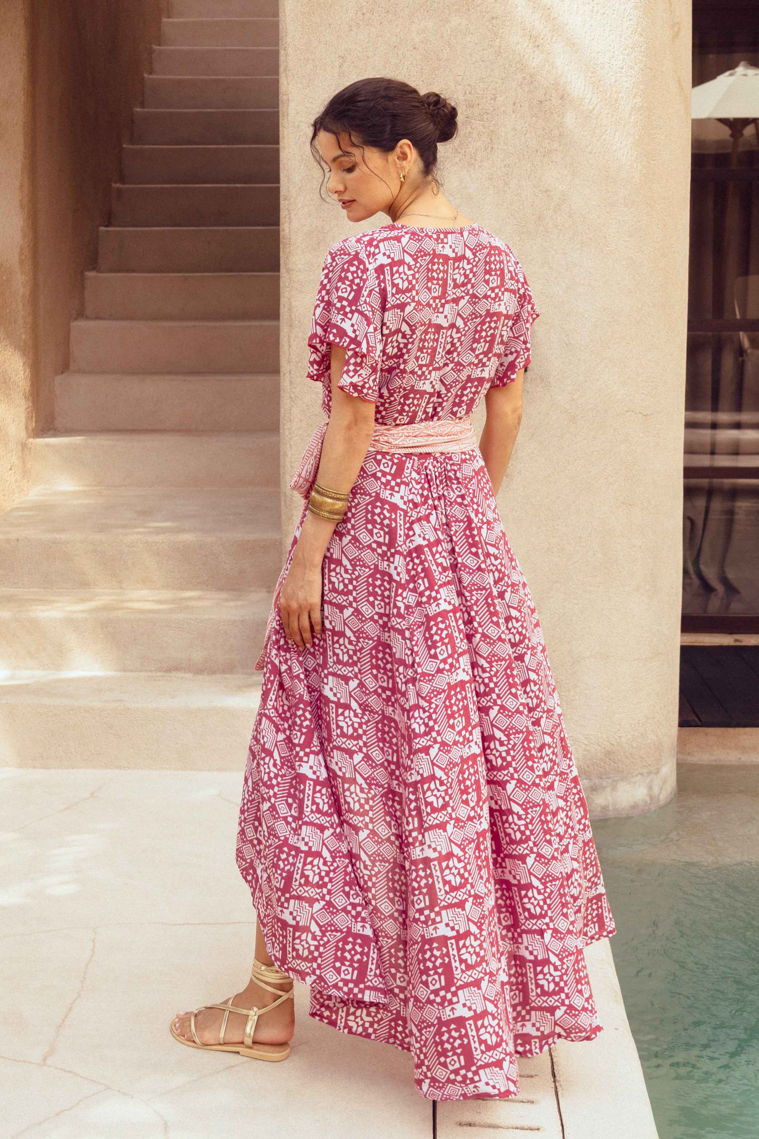 Woman in a pink floral dress standing by a poolside.