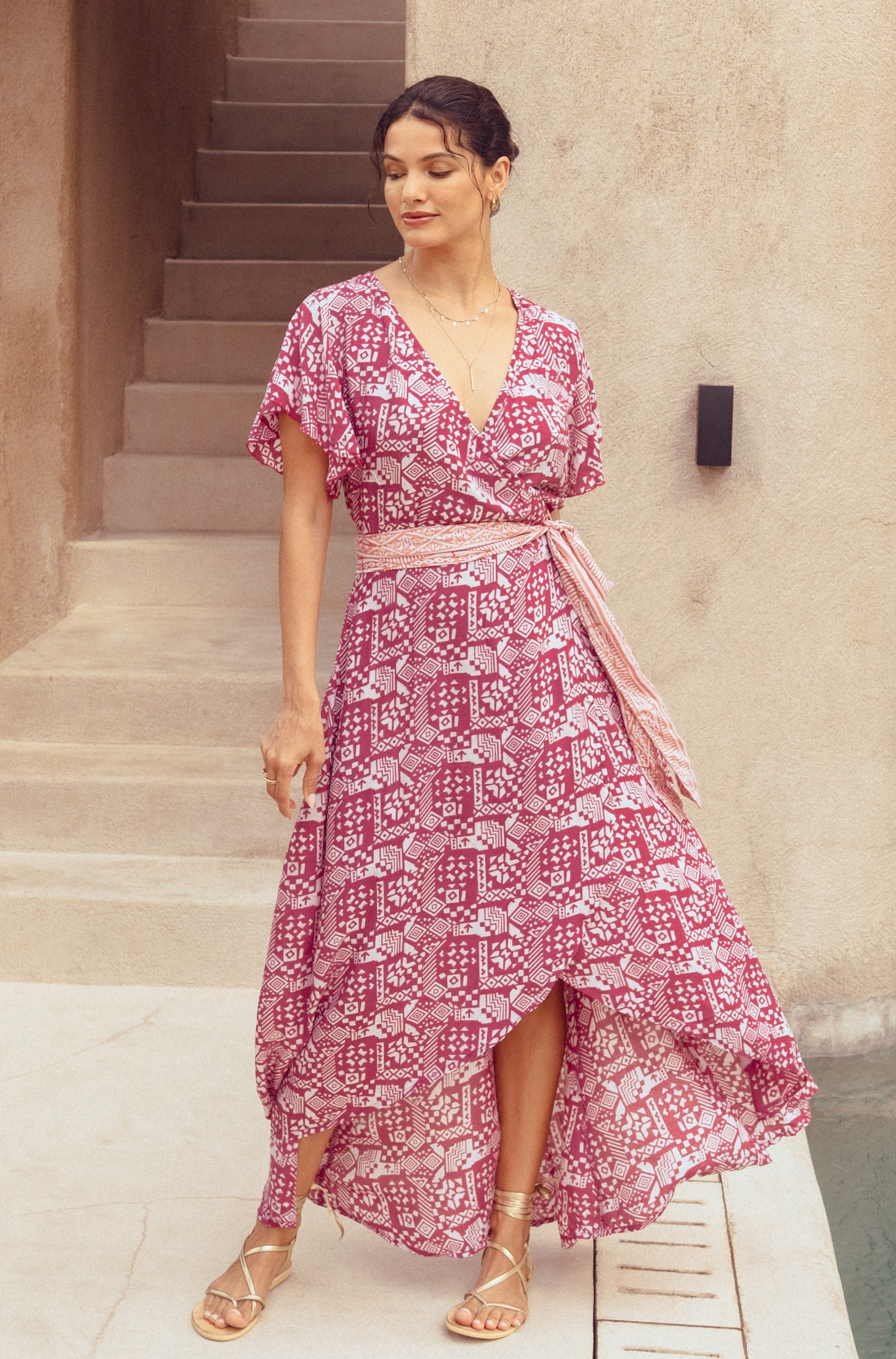 Woman wearing a pink patterned dress standing on a staircase.