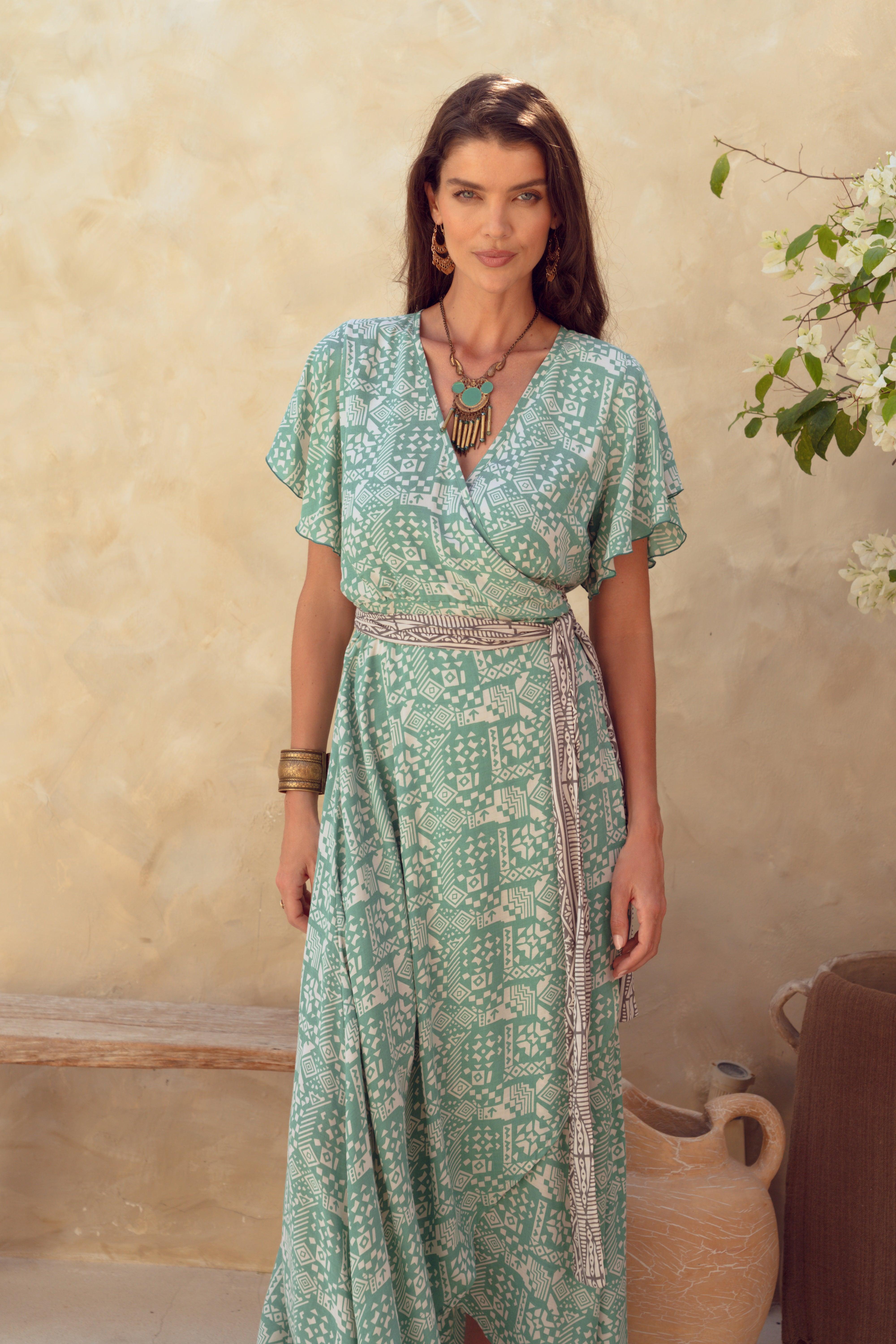 Woman wearing a green patterned dress standing against a beige wall with decorative elements.