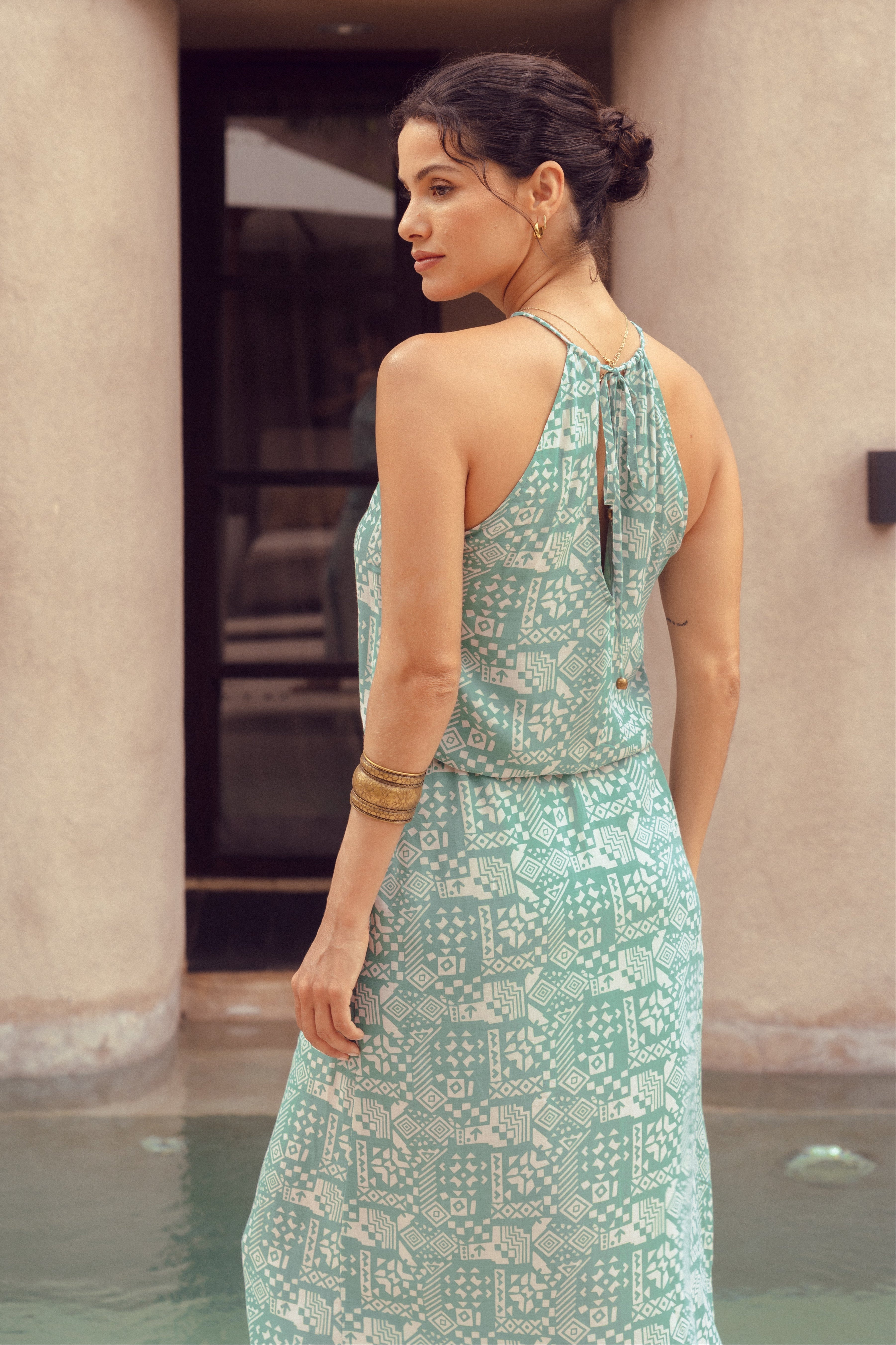 Woman in a green patterned dress standing by a pool with columns in the background