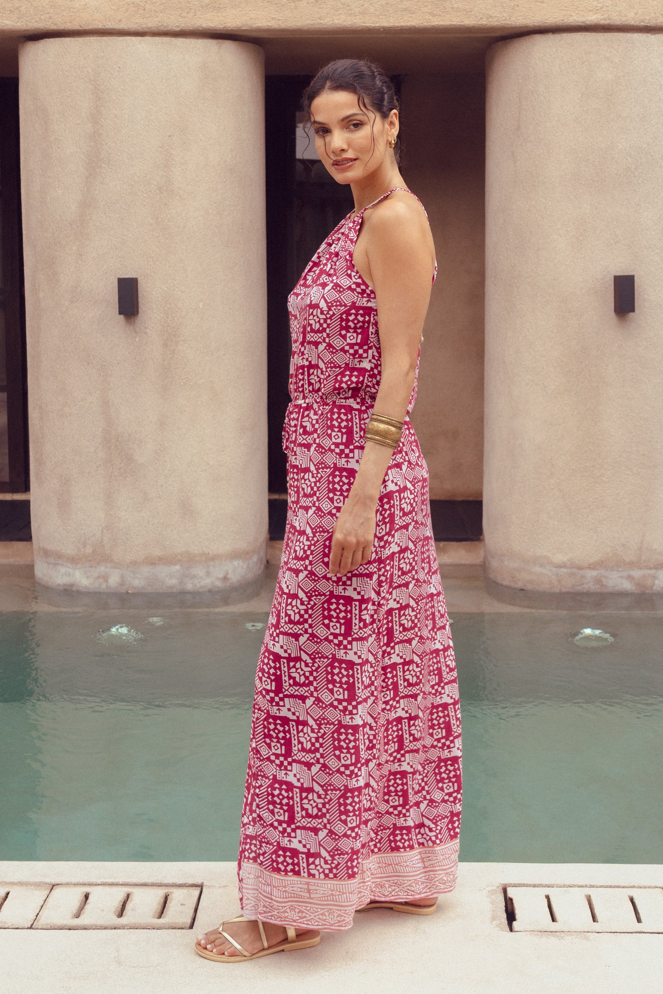 Woman in a pink dress standing by a pool with a modern building in the background