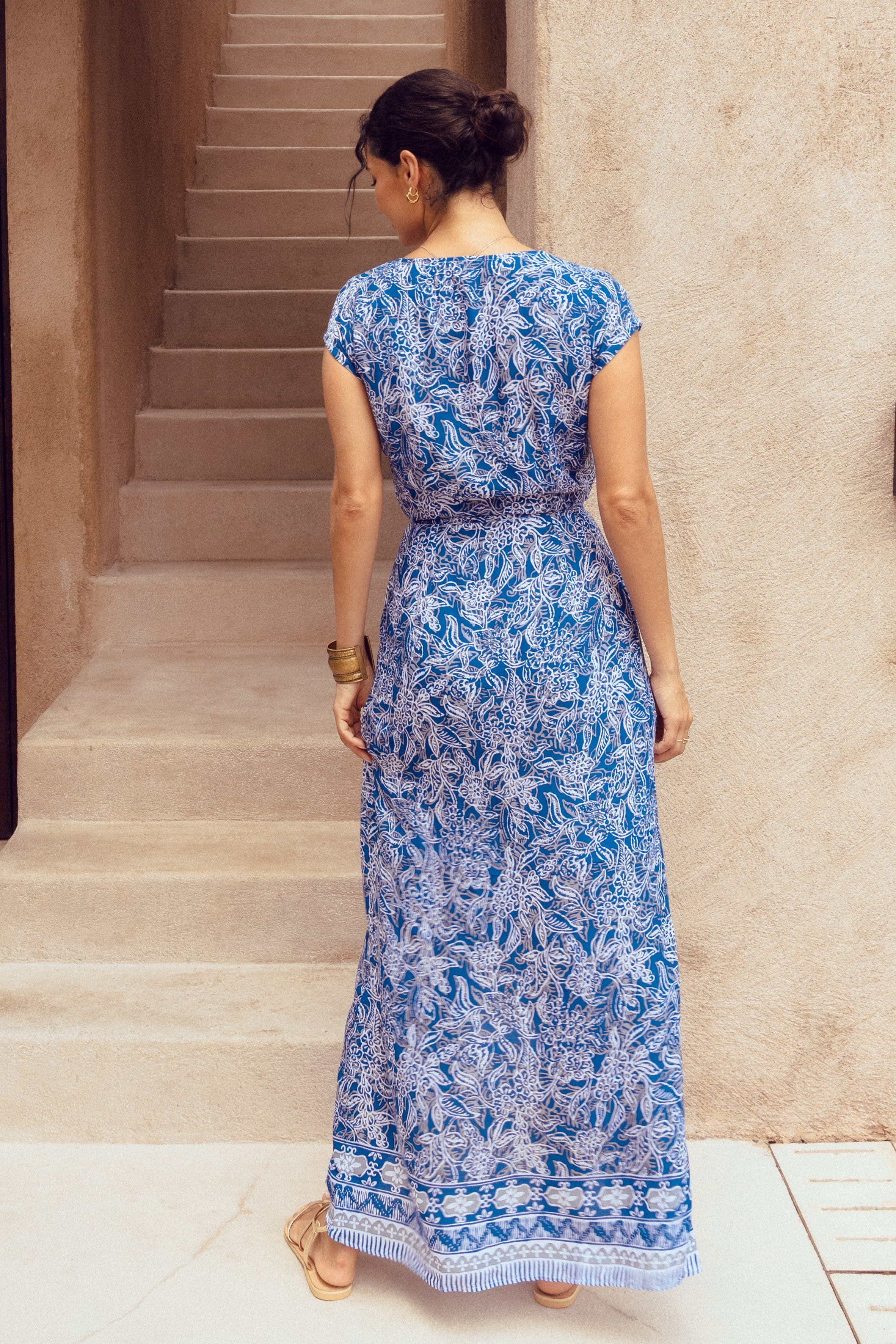 Woman in a blue floral dress standing in front of a villa.
