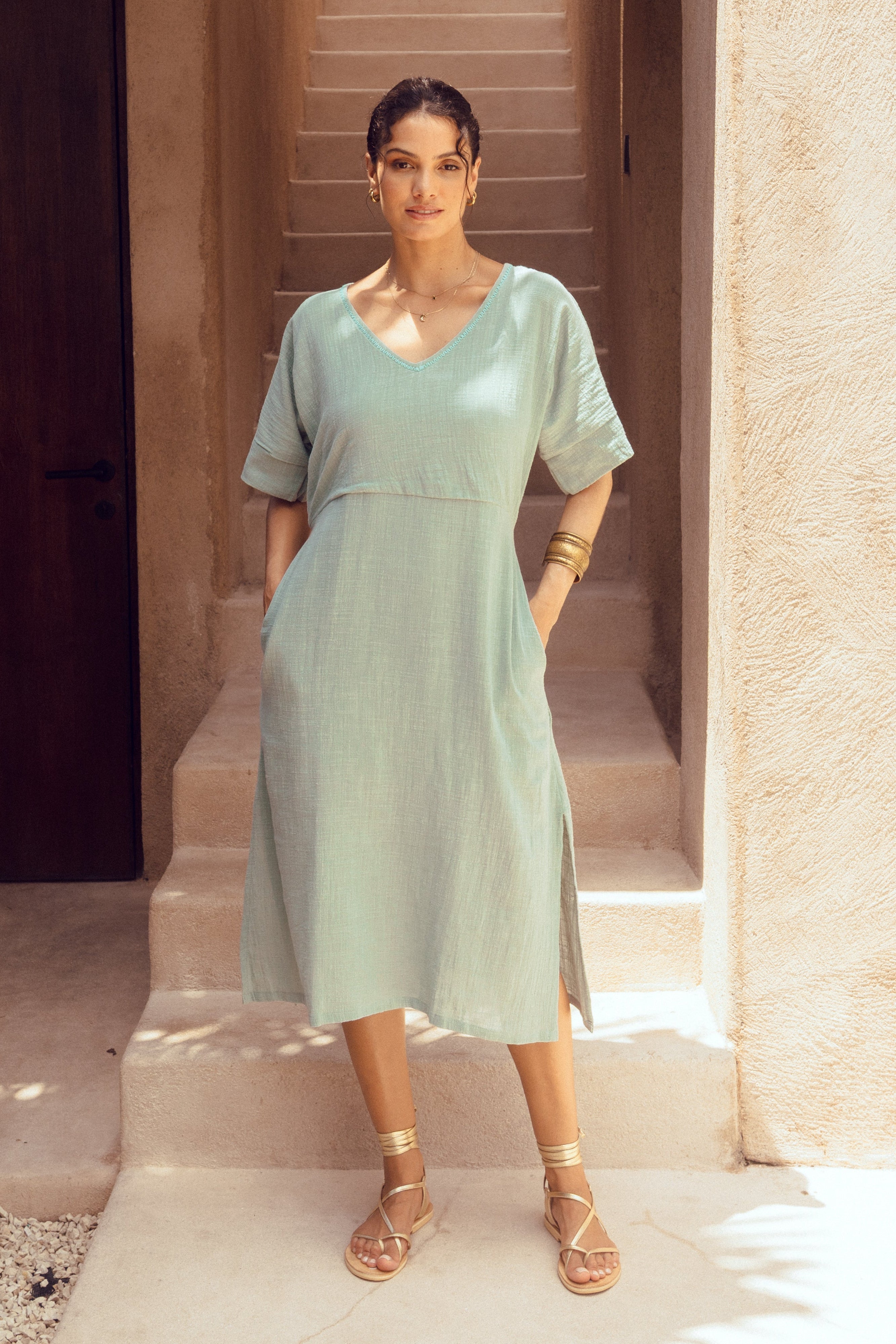 Woman in a light green dress standing in a sunlit architectural setting