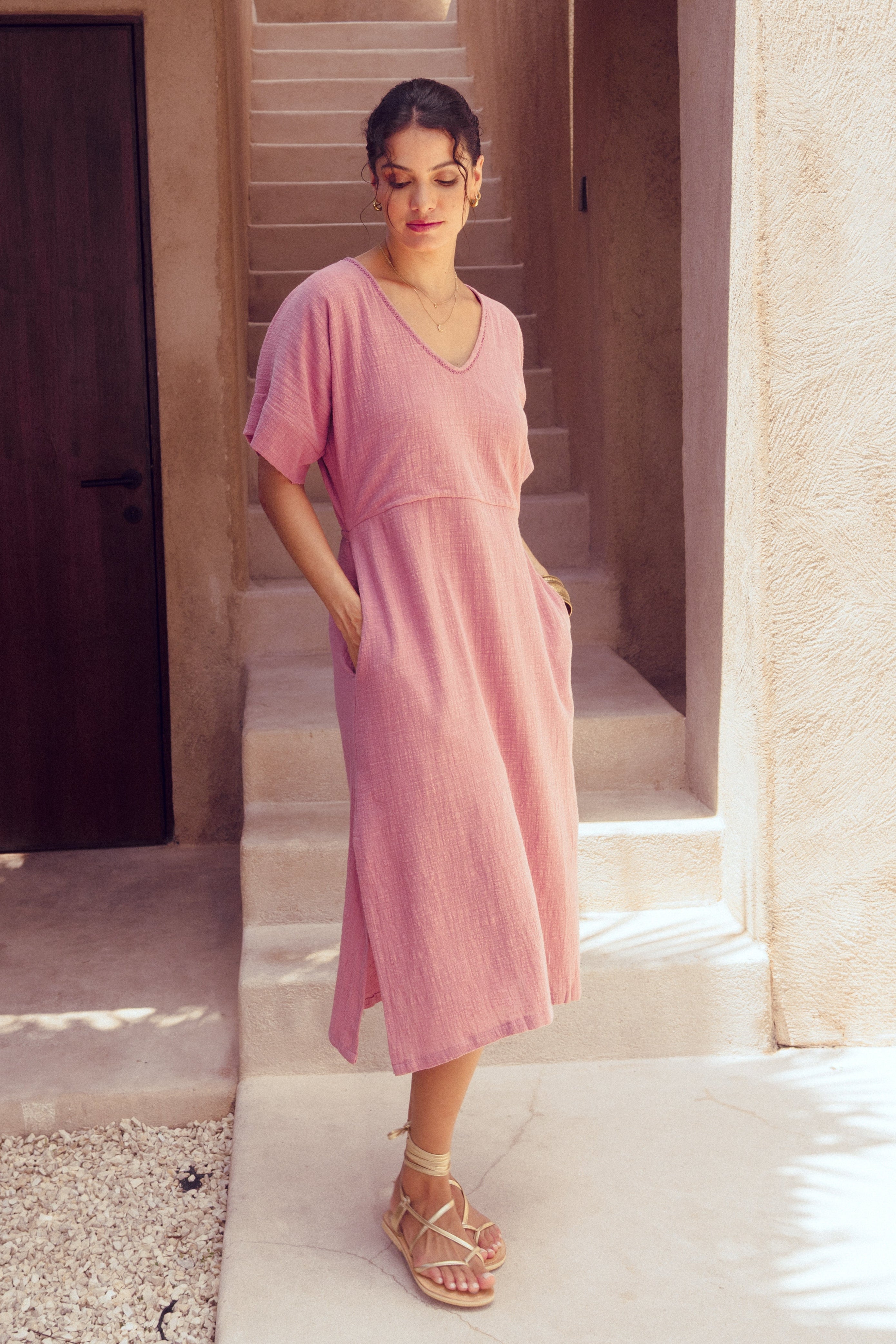 Woman in a pink cotton dress standing in a sunlit hallway at a villa