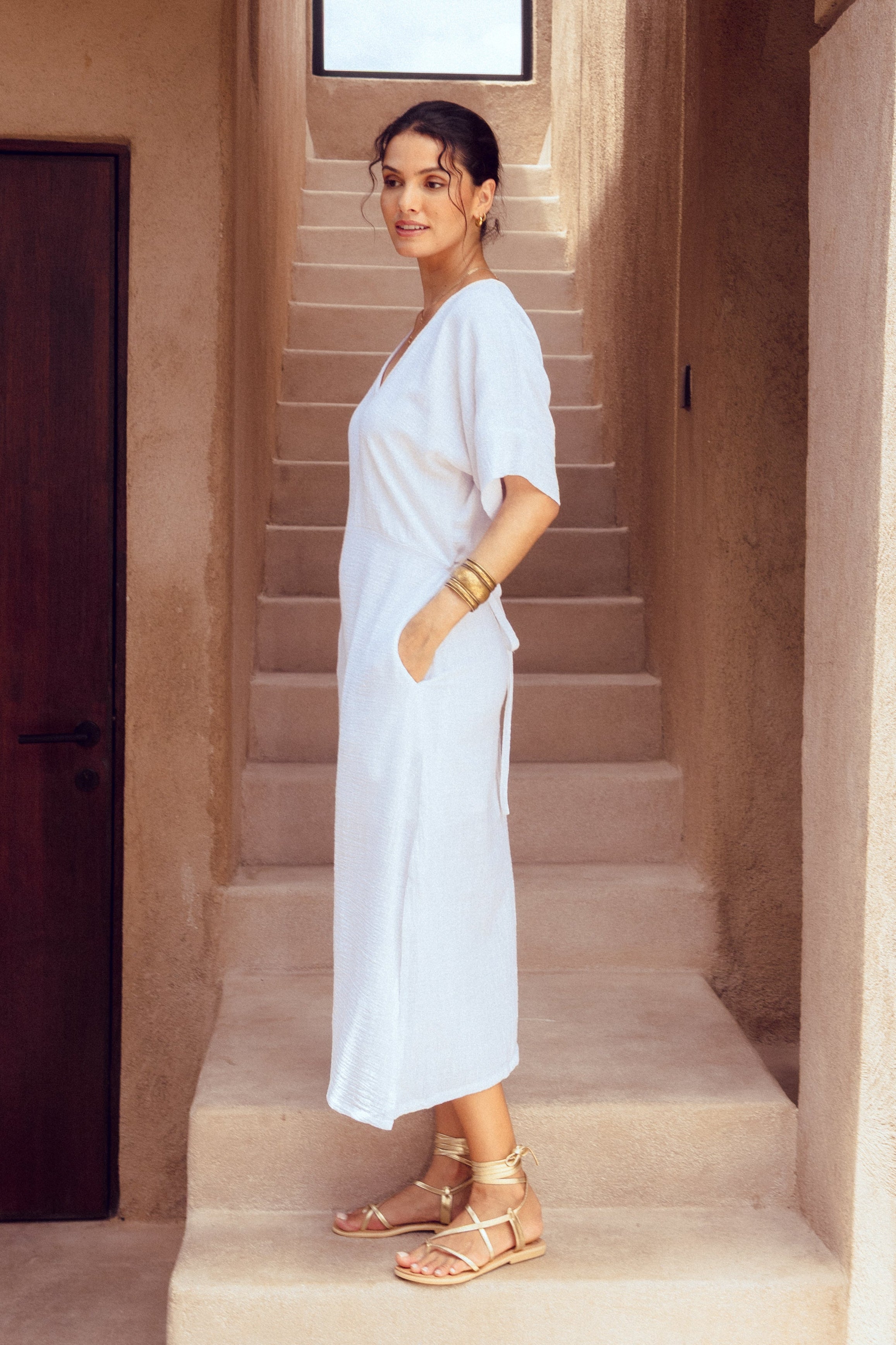 Woman in a white dress standing on steps in a sunlit architectural setting