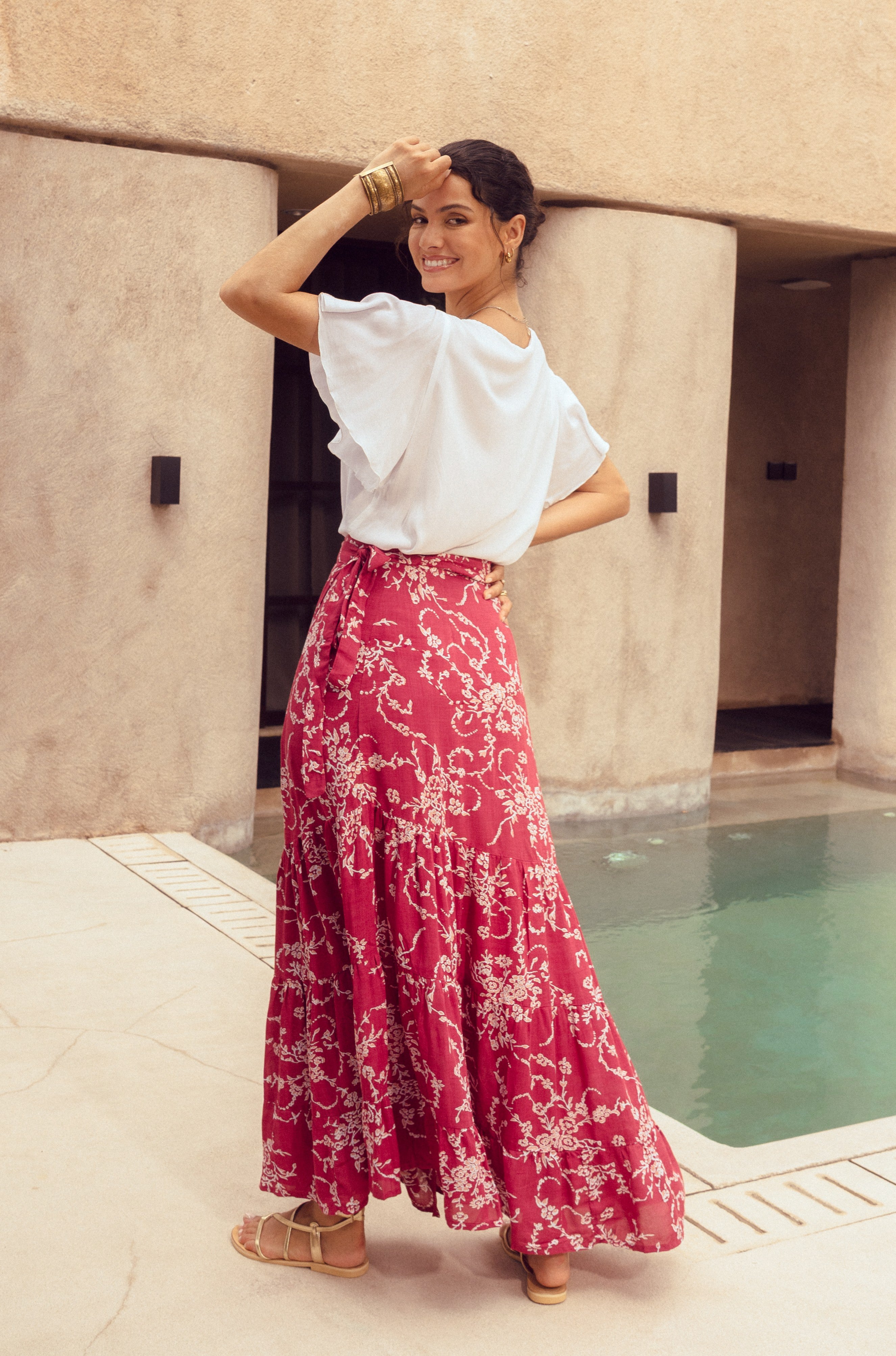 Woman in a white top and red floral skirt standing by a poolside.