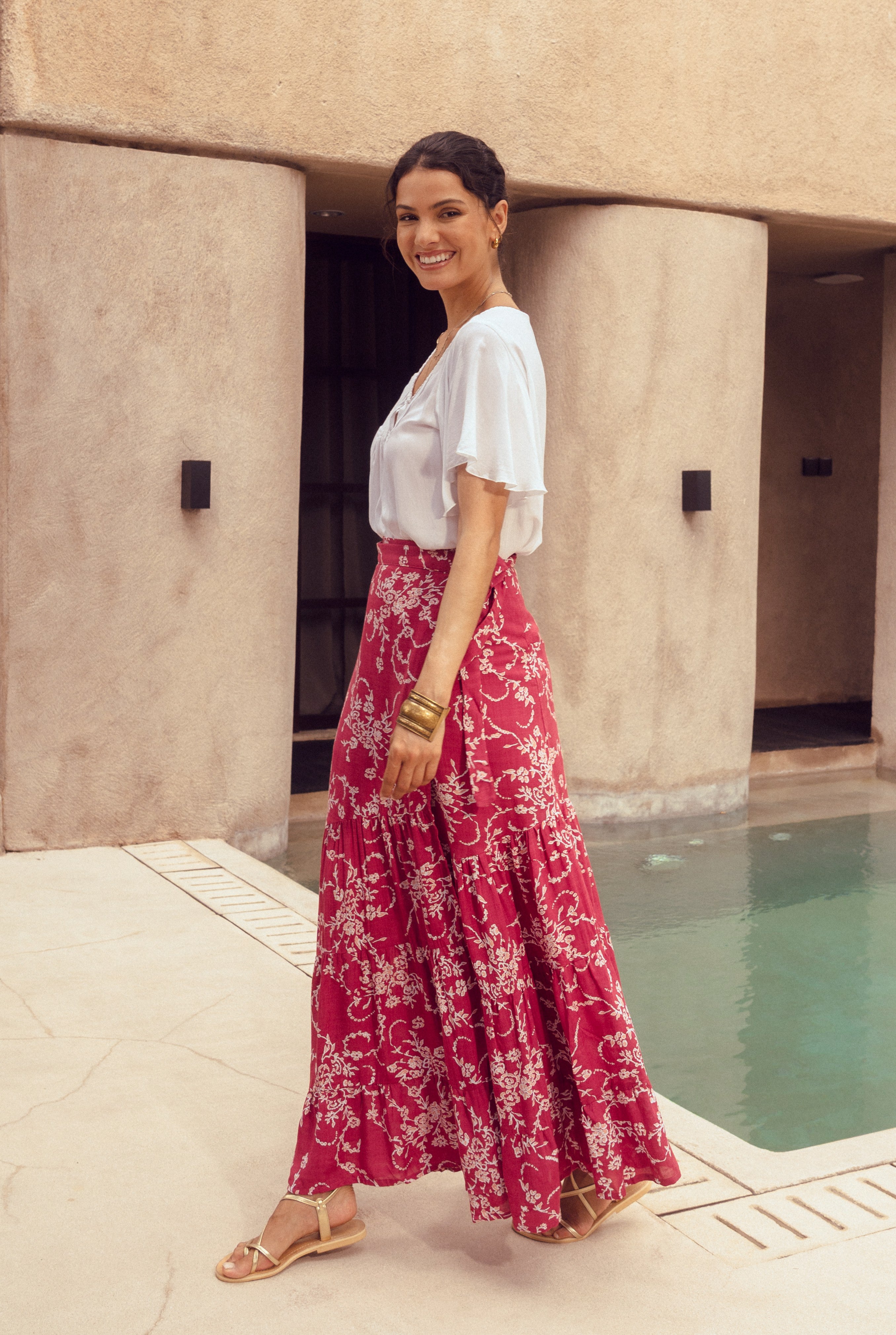 Woman in a white top and red floral skirt standing by a poolside.