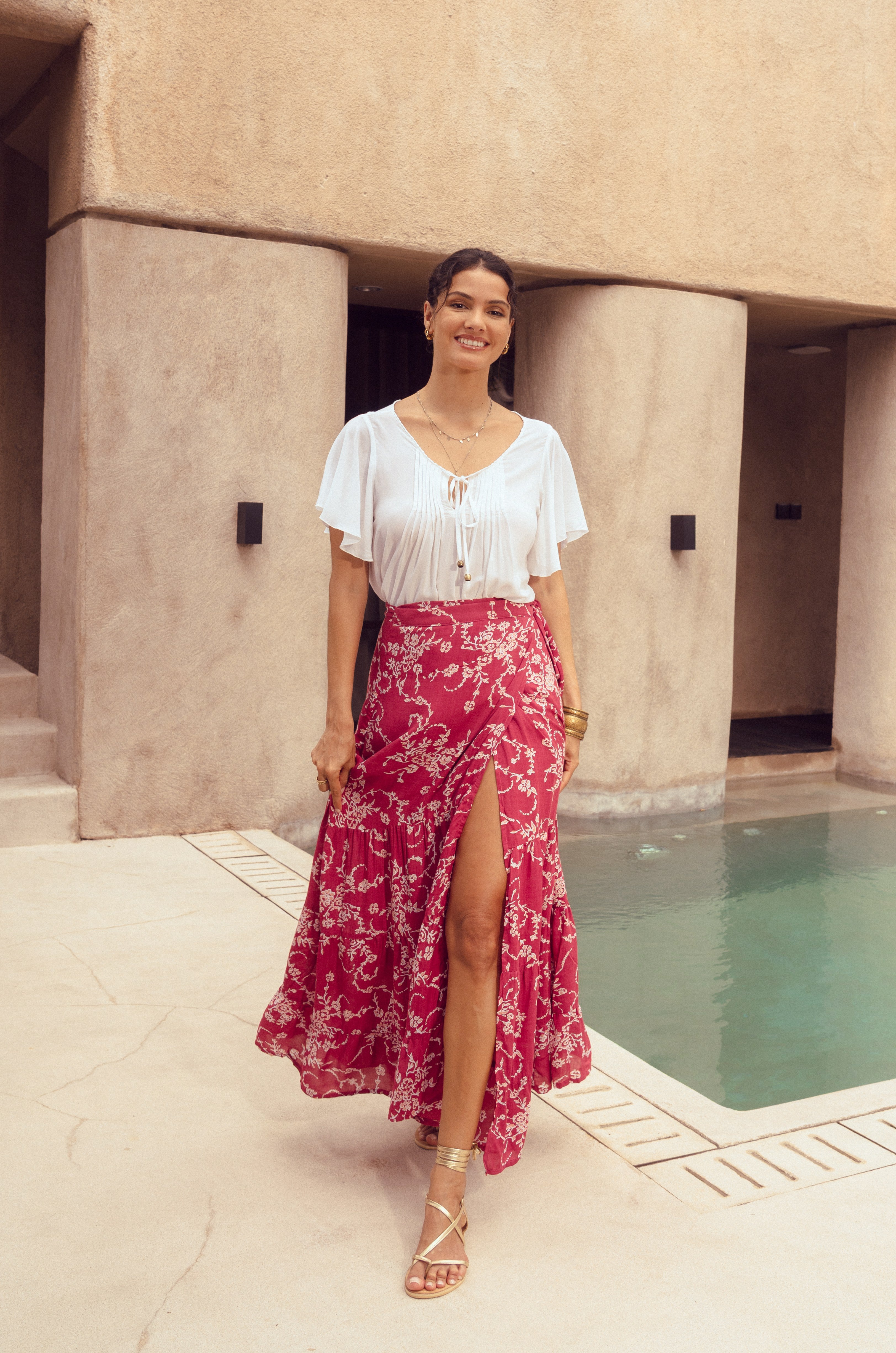 Woman in a white blouse and red floral skirt standing by a poolside.