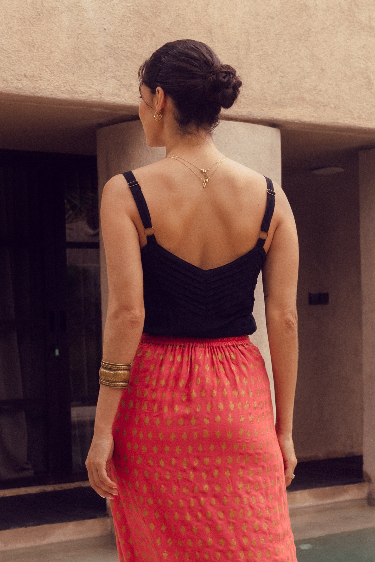 Woman in a black top and red skirt standing by a poolside building.