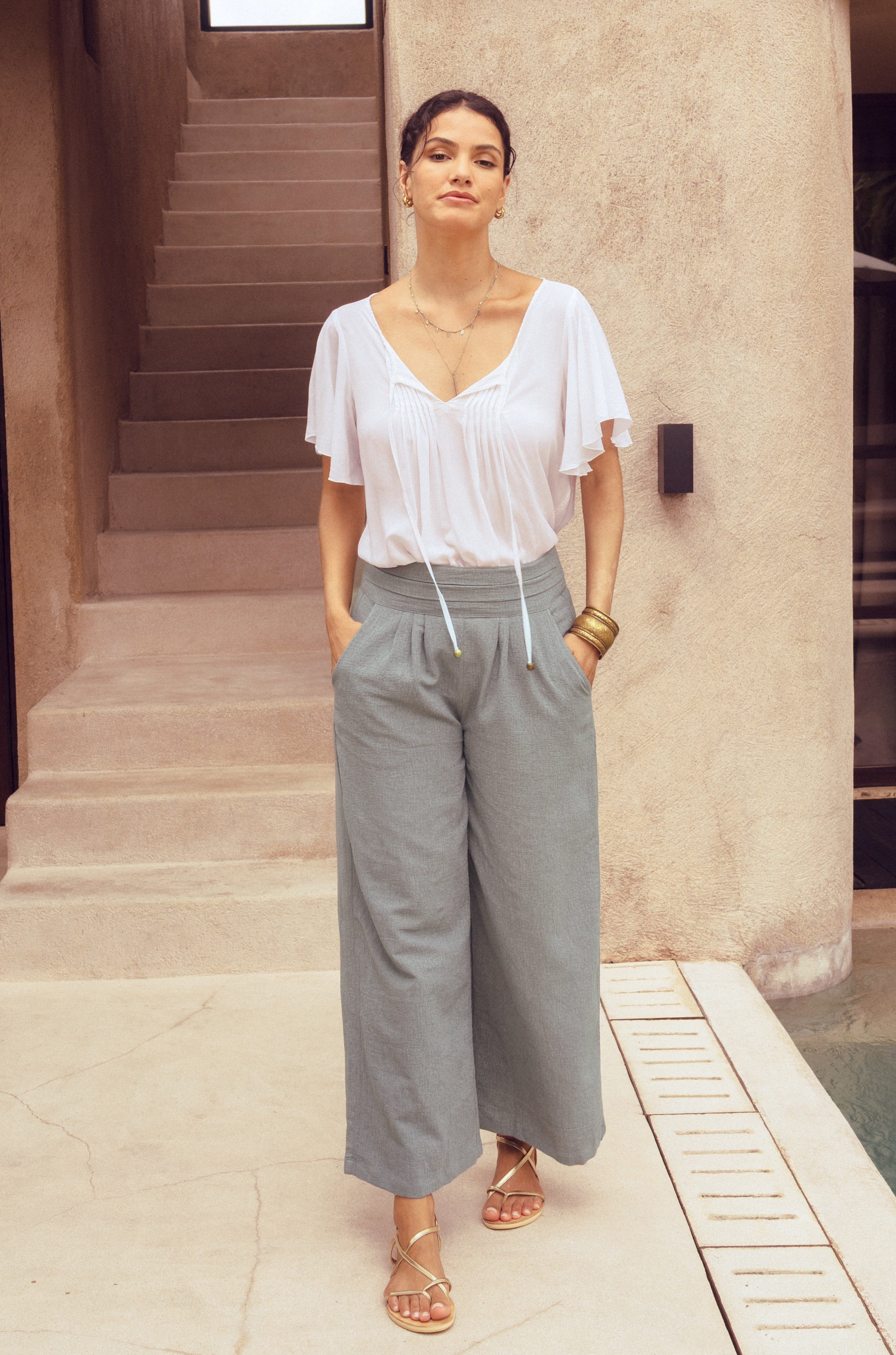 Woman wearing a white blouse and gray wide-leg pants standing in front of a building.