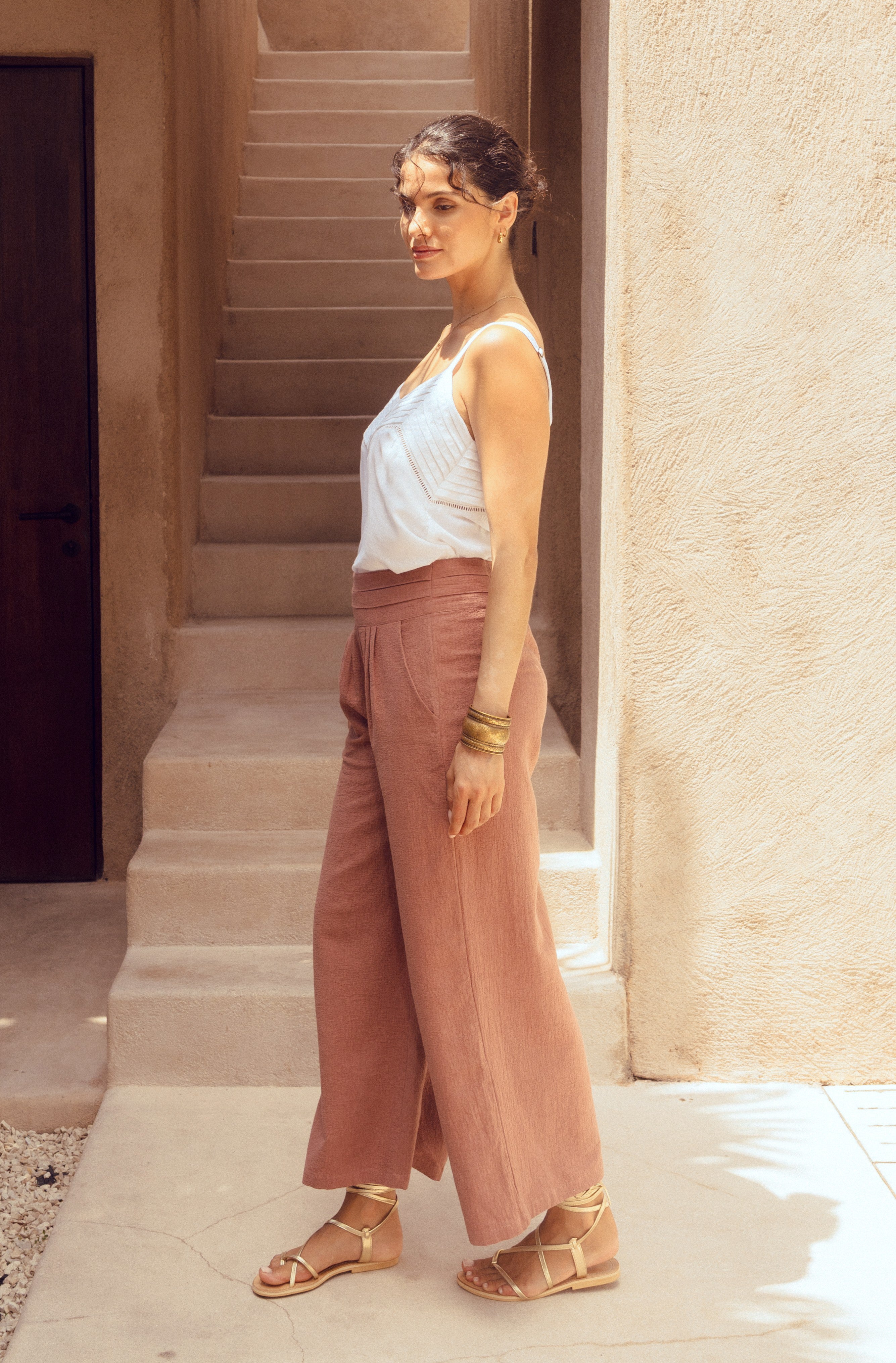 Woman in white top and pink pants standing on a stone staircase.