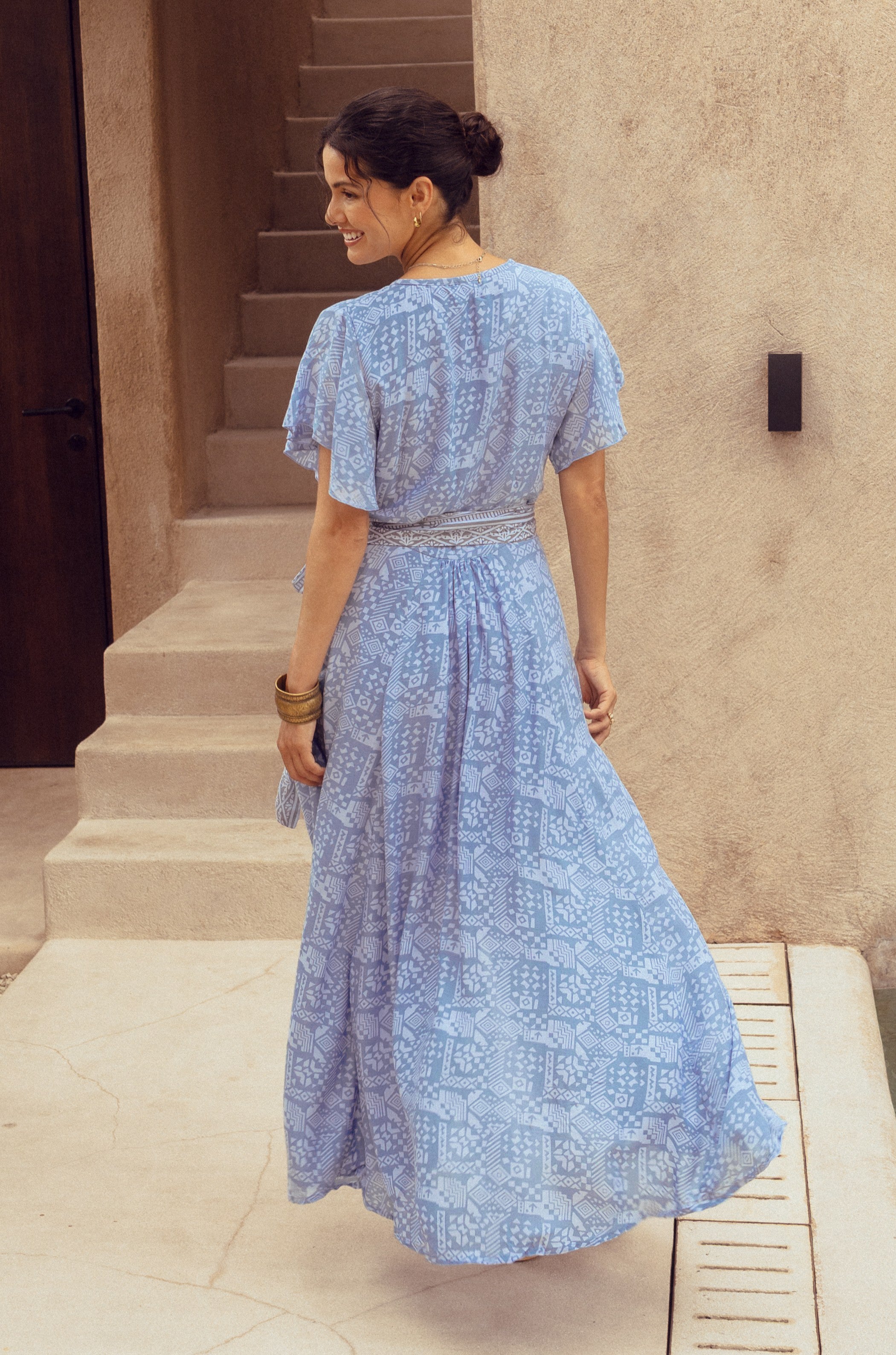 Woman in a blue patterned dress standing on a staircase.