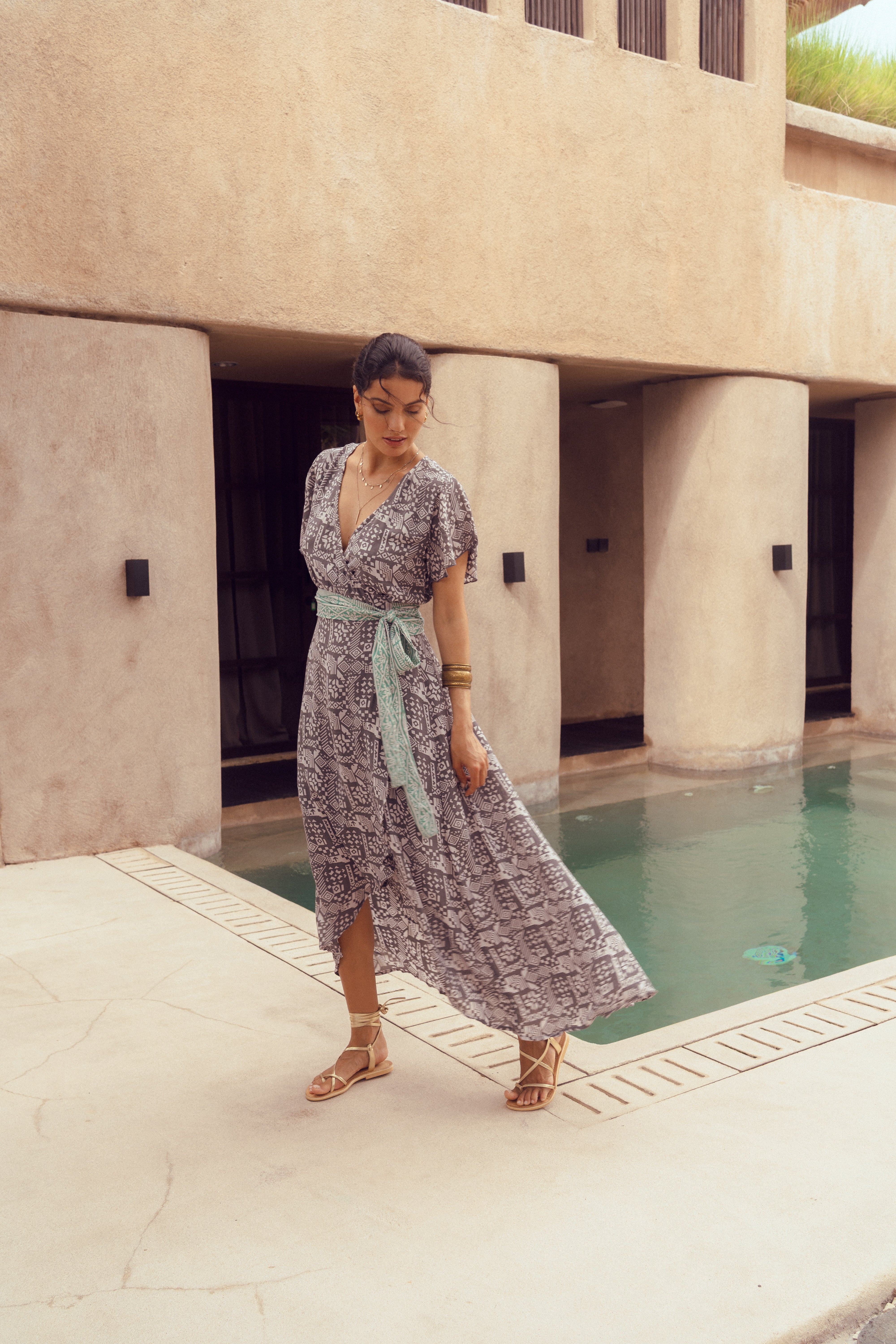 Woman in a patterned dress standing by a pool with a modern building in the background