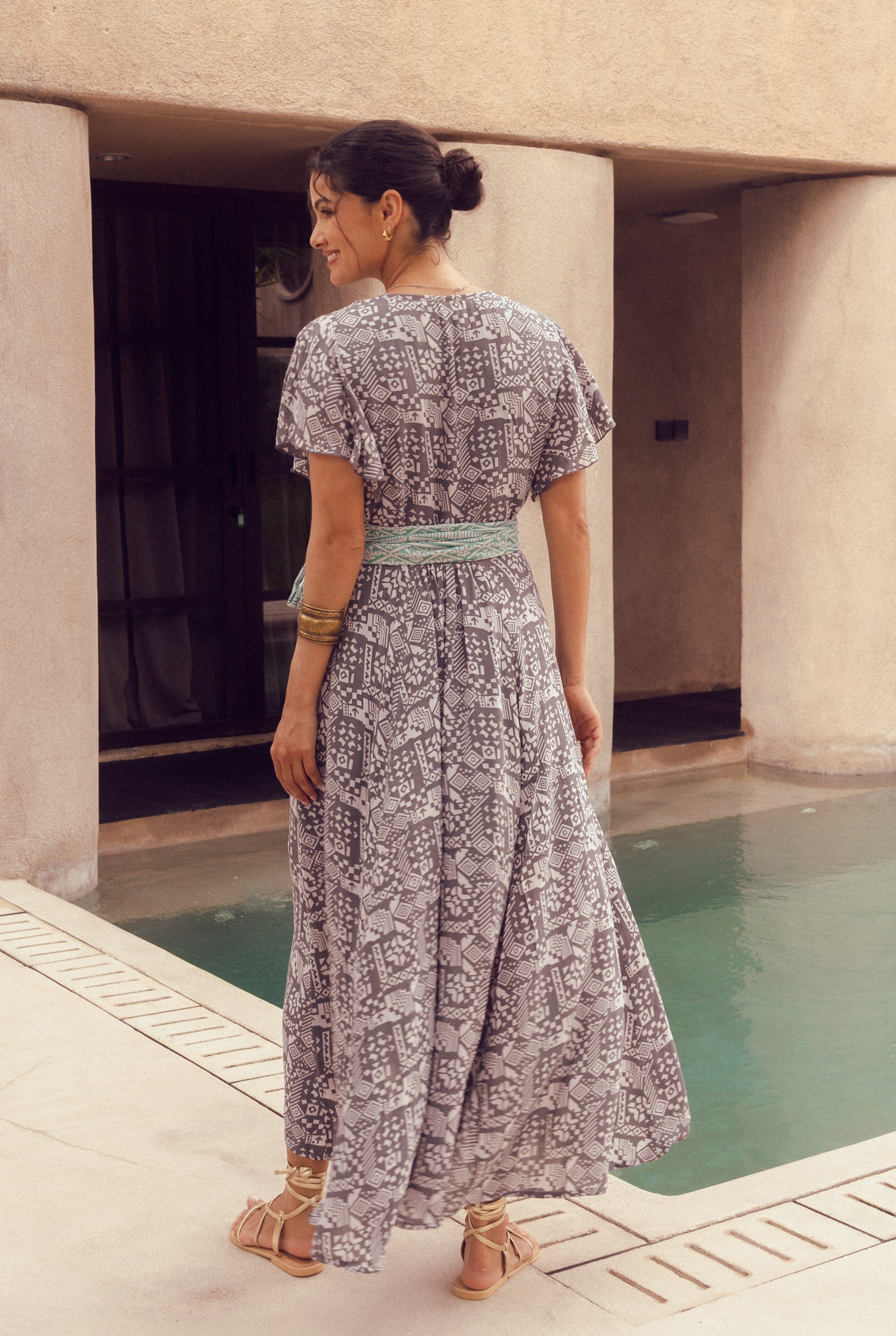 Woman in a patterned dress standing by a pool with columns in the background