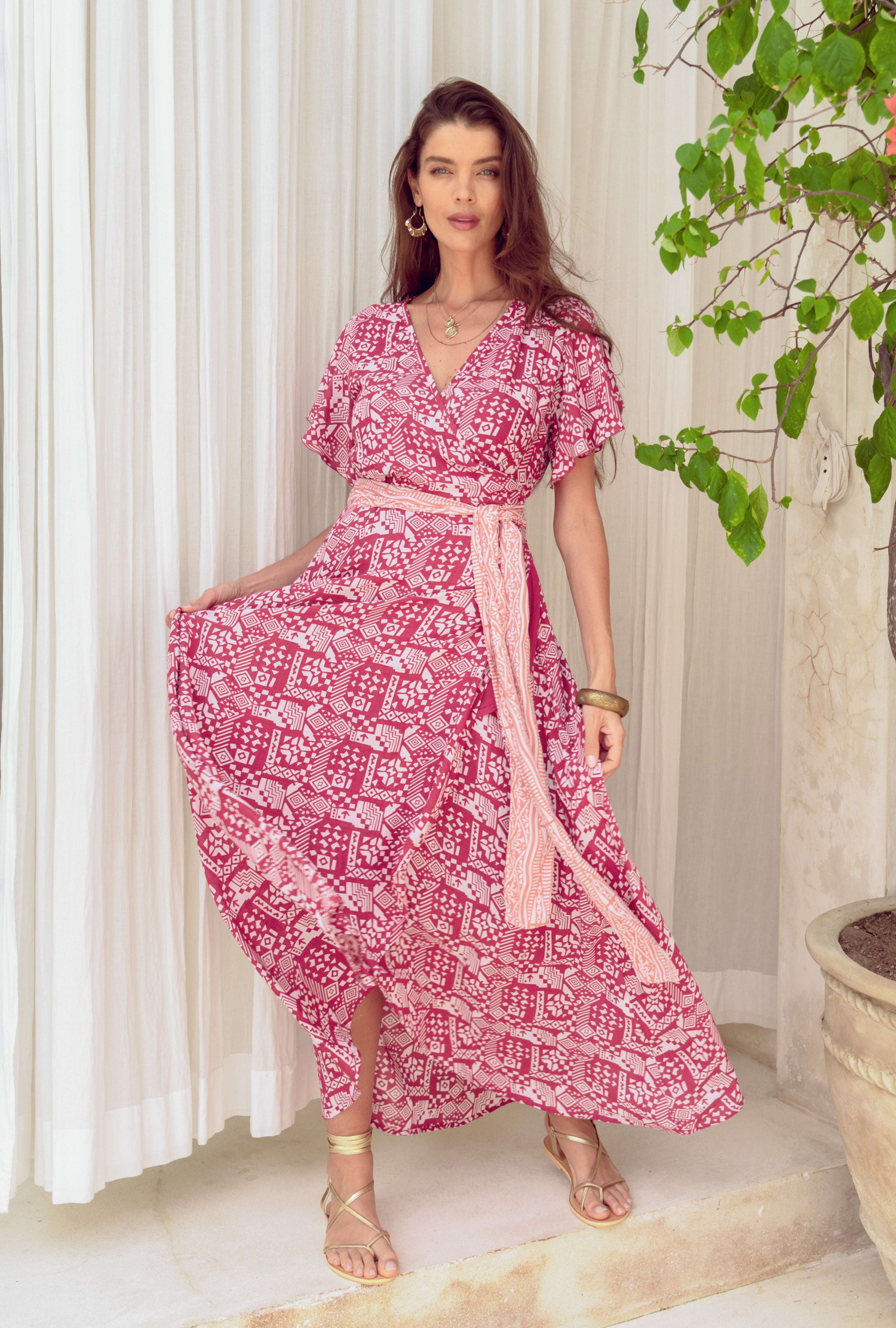 Woman wearing a pink patterned dress with a scarf in a bright room.