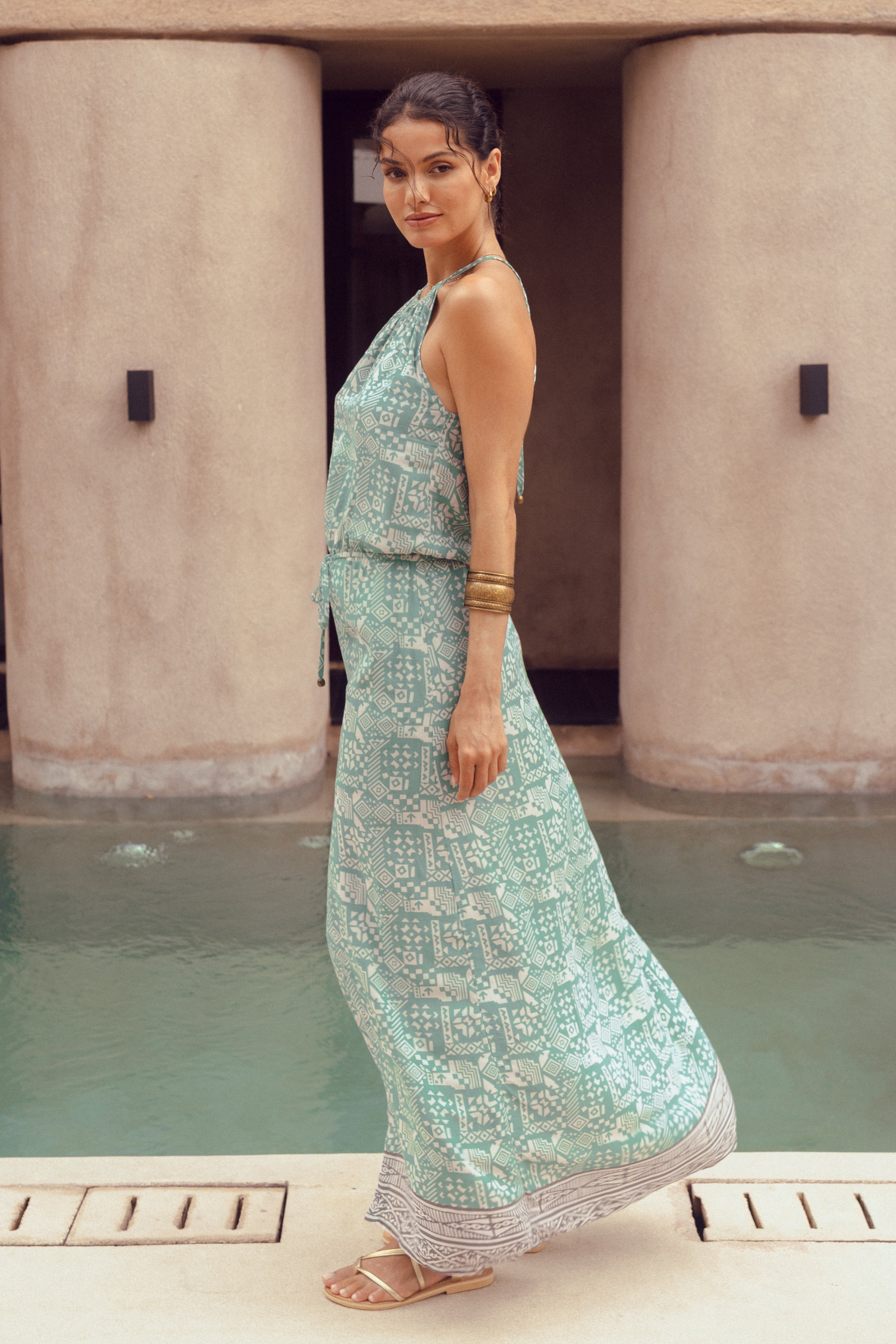 Woman in a light blue dress standing by a pool with a building in the background