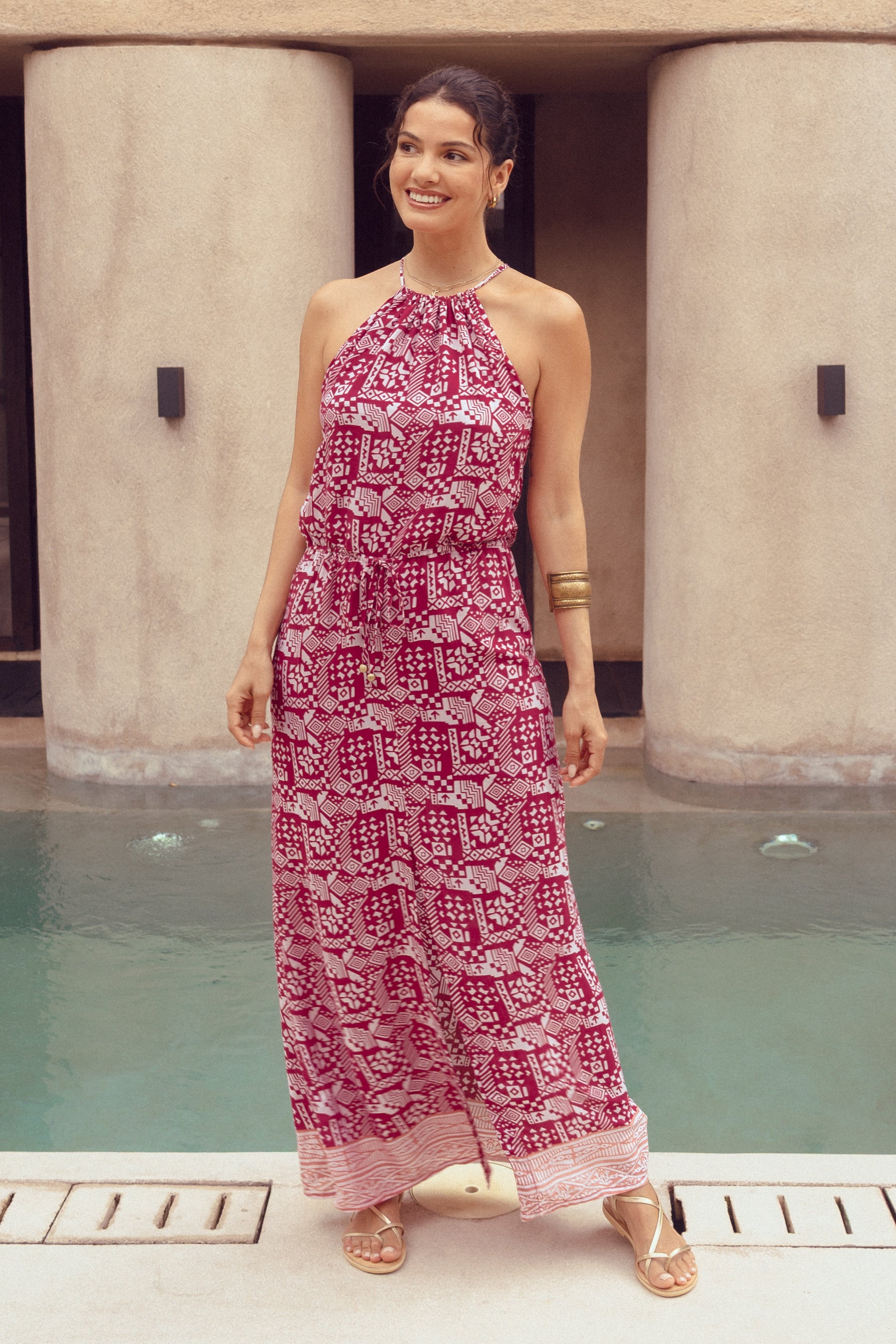 Woman in a pink patterned dress standing by a pool with a modern building in the background
